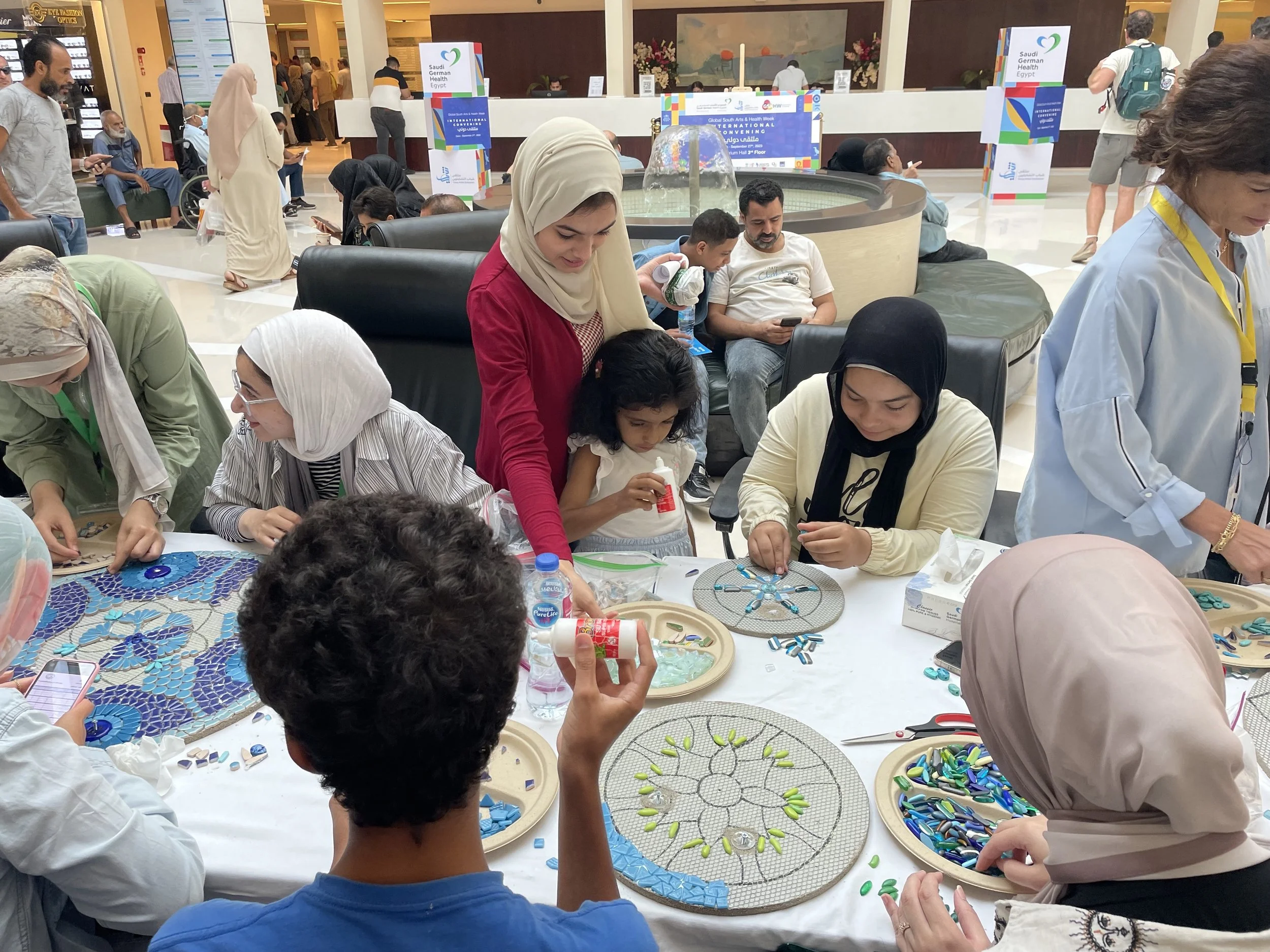 A group of children and adults glue tiles to mosaic circles