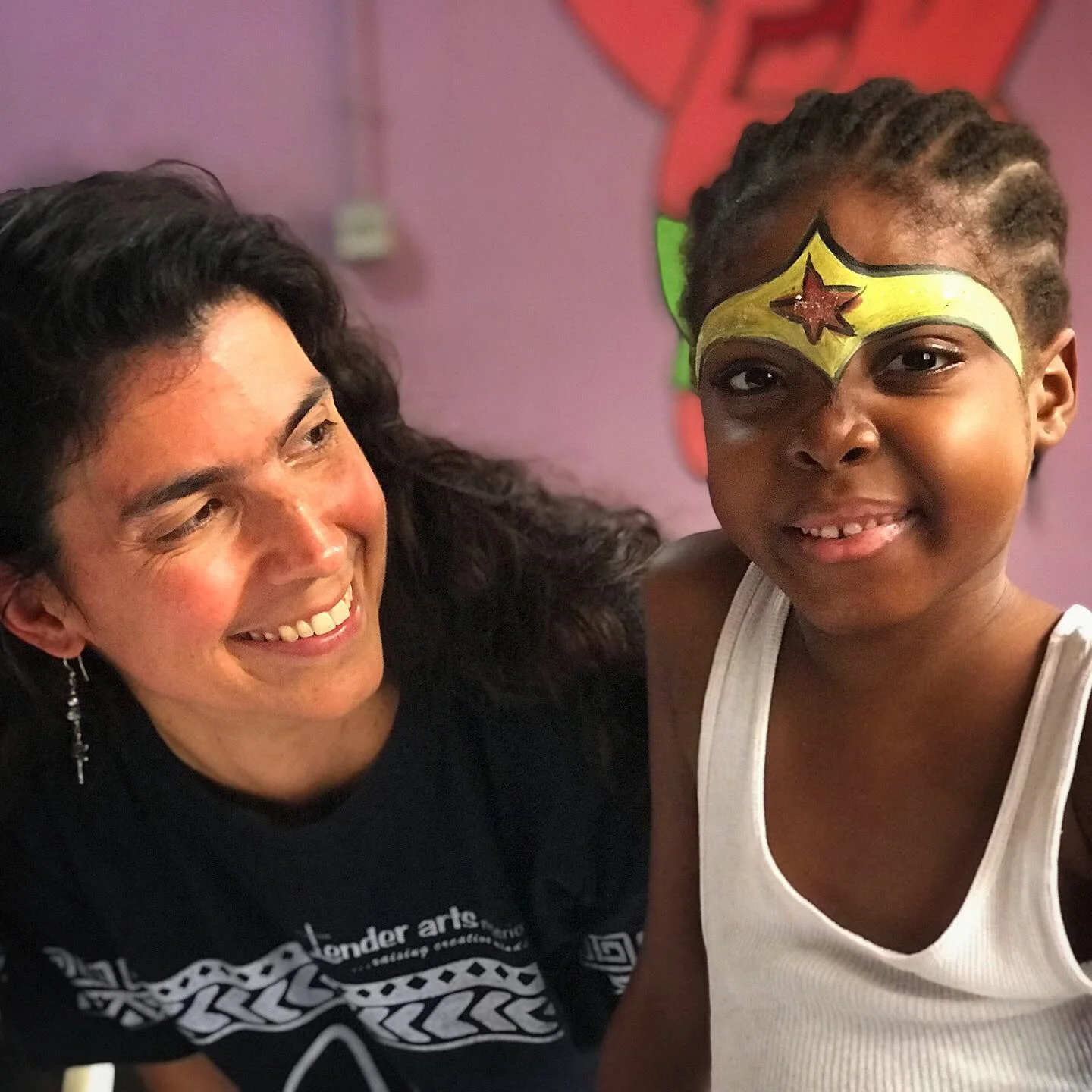 A woman smiles at a girl who is happy with a face painted crown 