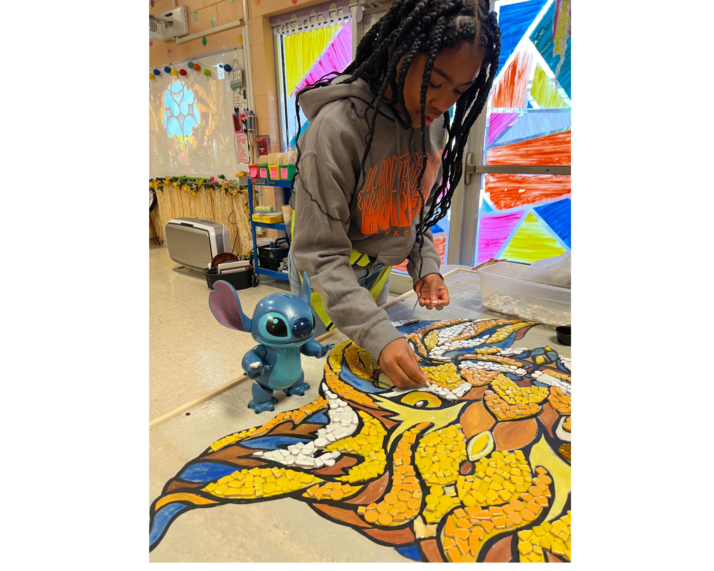 A young girl works on a mosaic while.a stitch figurine looks on 