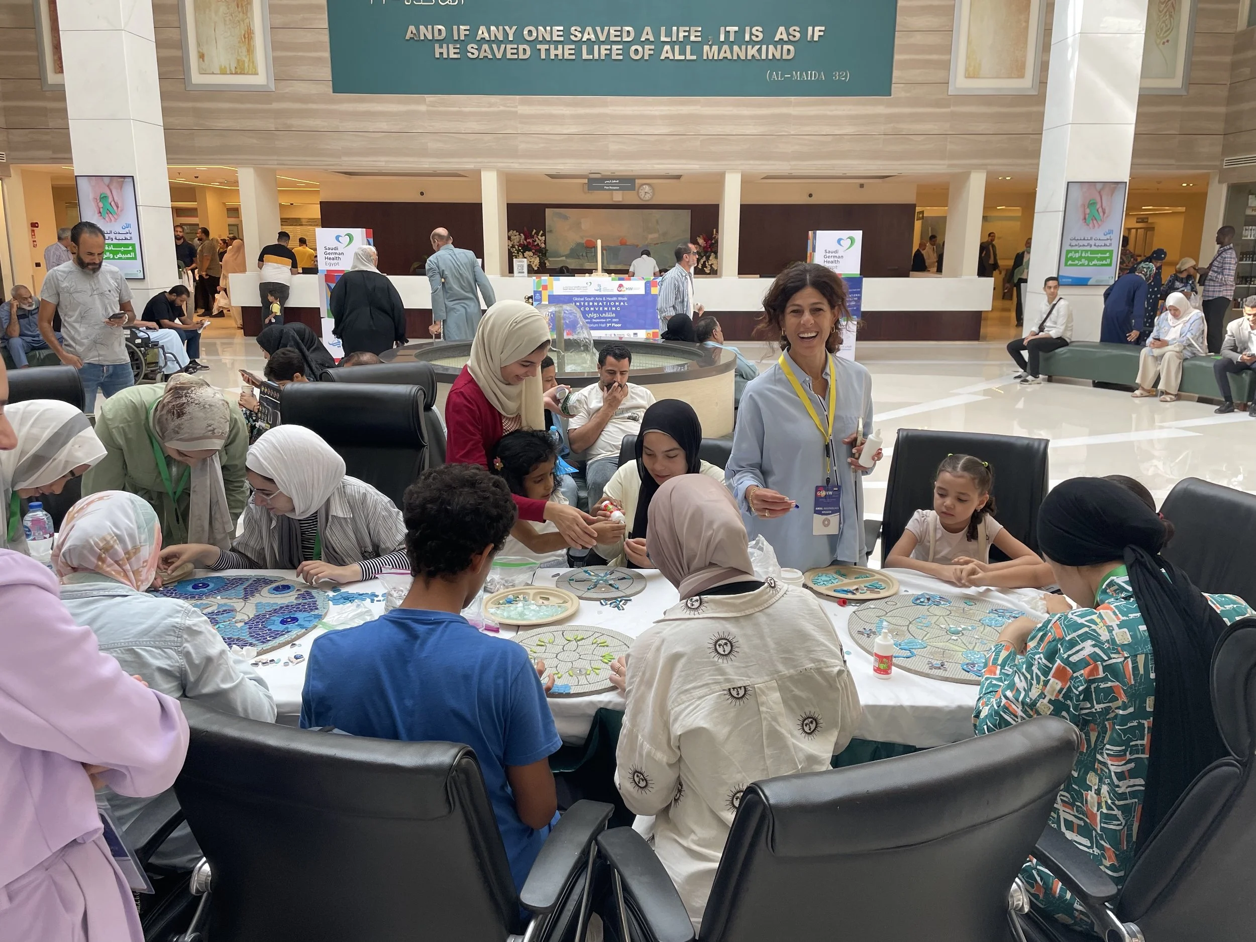 A large group of people in a hospital lobby work on a collaborative art project 