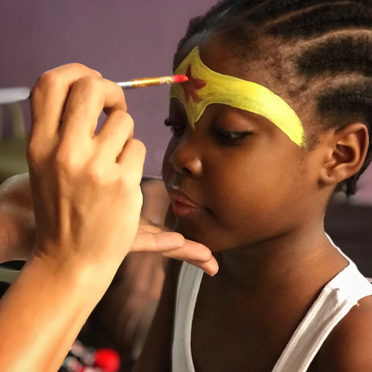 A little girl gets face paint of a superwoman crown