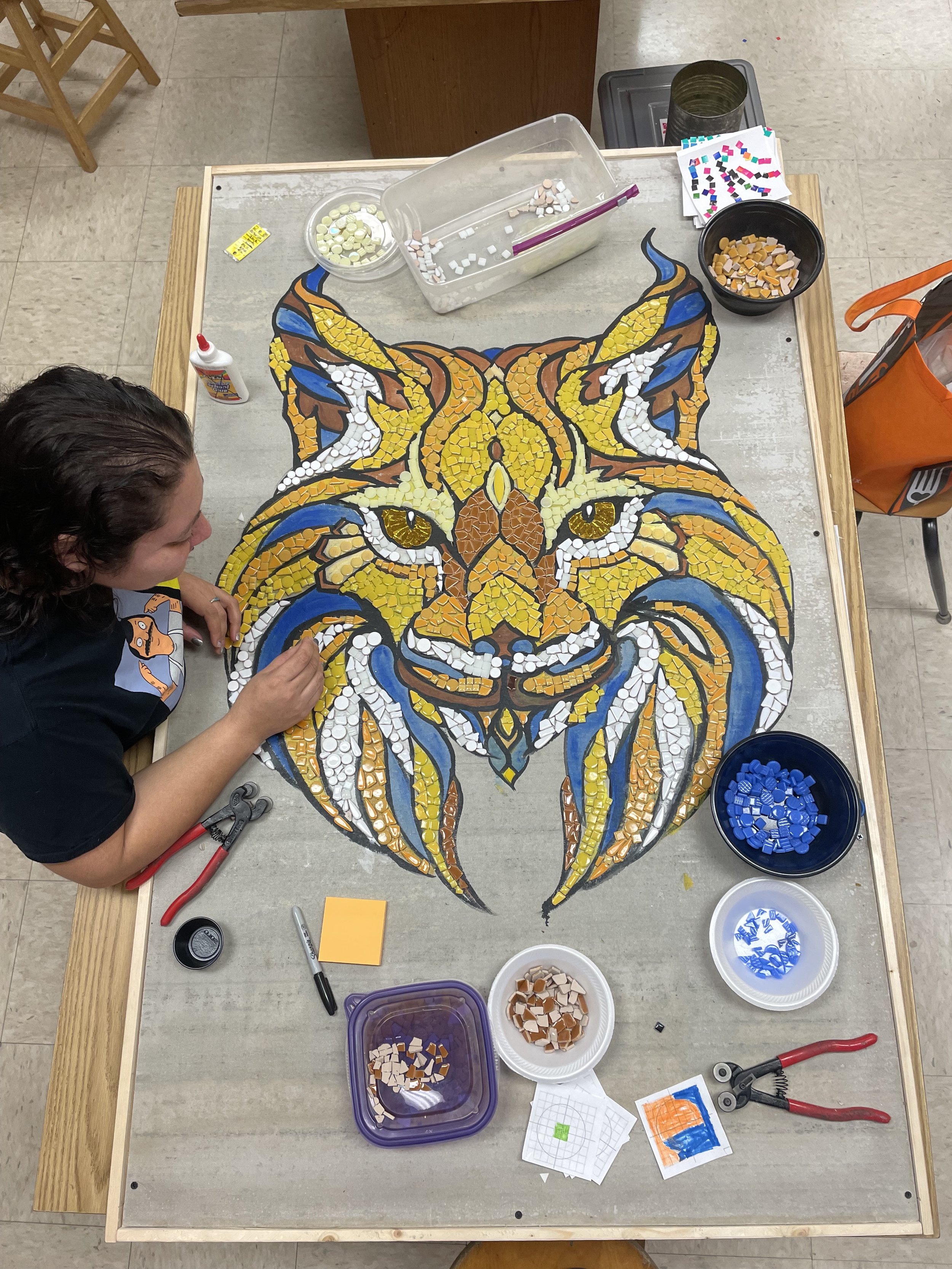 an art teacher touches up student mosaic work of a fierce wildcat 