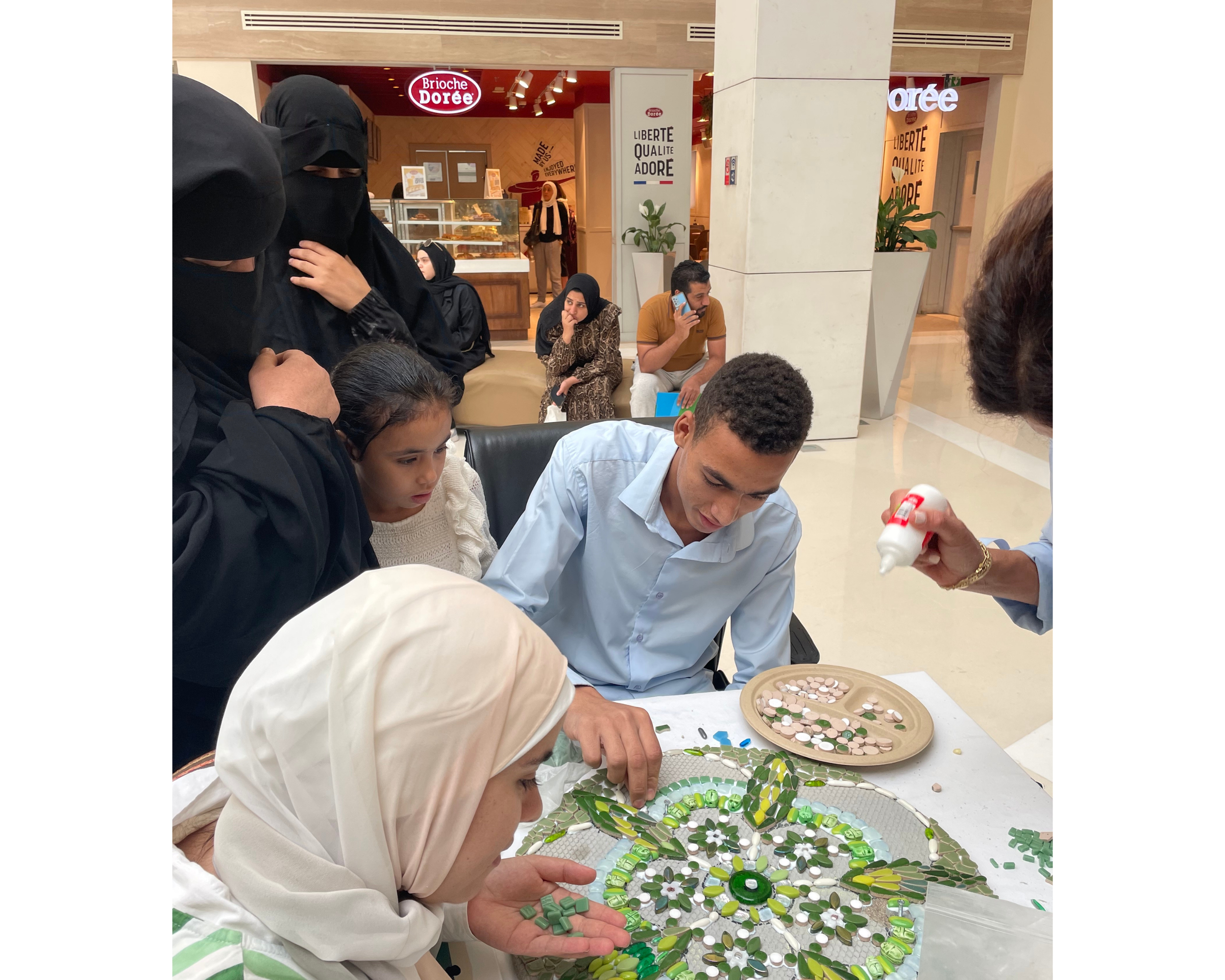 Two women in black burkas and a child watch a man and woman create a mosaic 