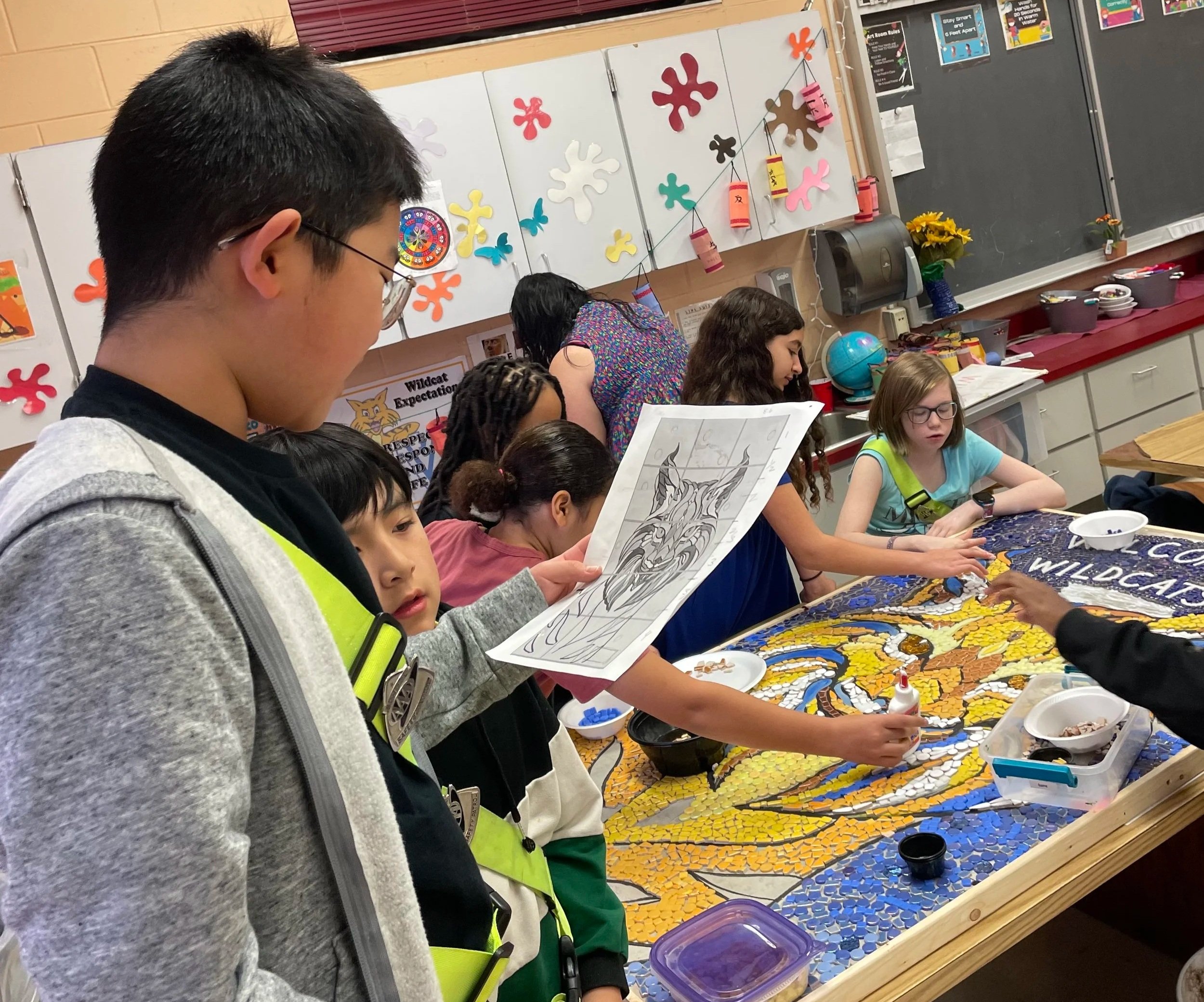 A boy interprets a sketch while his classmates make a mosaic mural