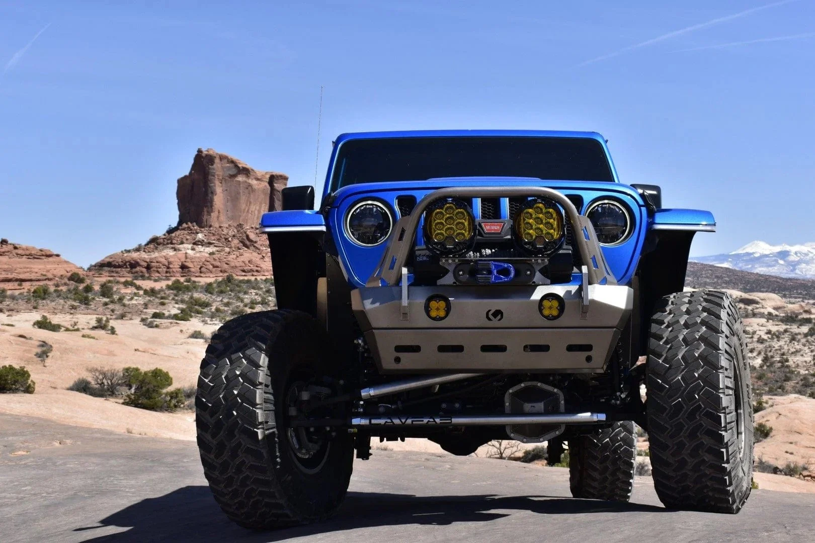 A Close up of a blue jeep in the desert to feature its lift kit and suspension
