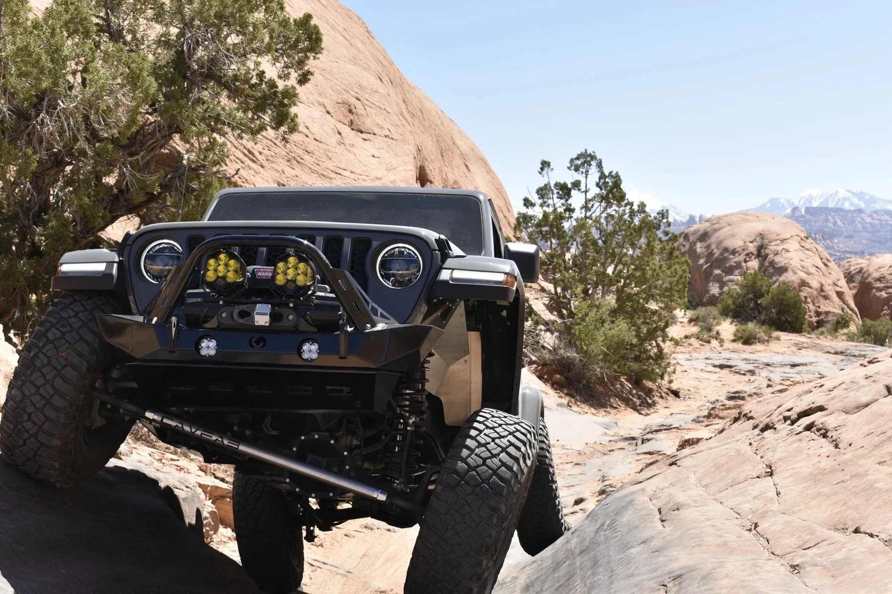 Close up of the front grill of a gray jeep off roading up a hill