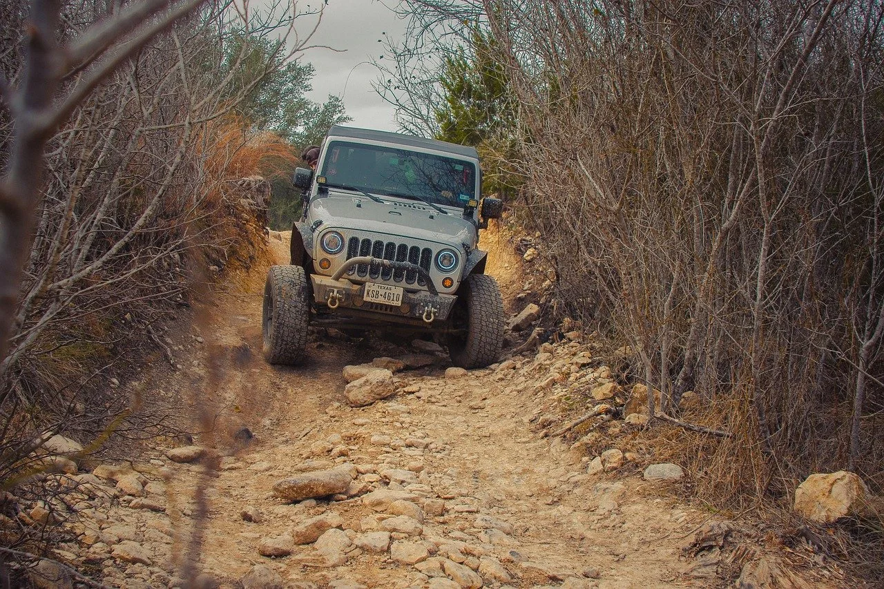 A gray lifted Jeep Wrangler going down a trail of rocks