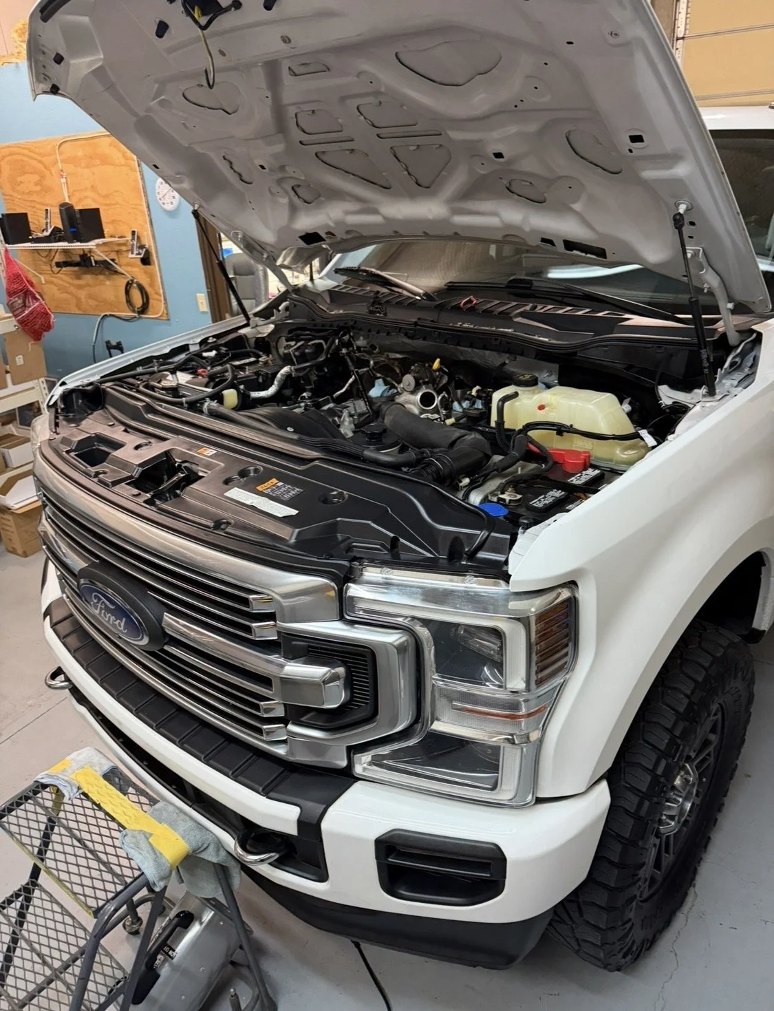 White Ford pickup truck with its hood open, showing the engine compartment in a garage.