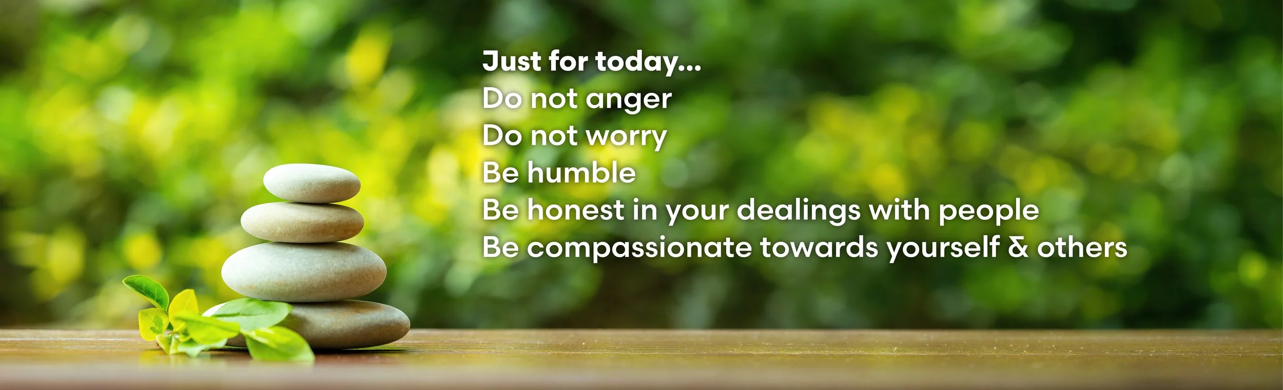 A balanced stack of stones on a wooden surface with green foliage in the background, overlaid with an inspirational message about humility, honesty, and compassion.
