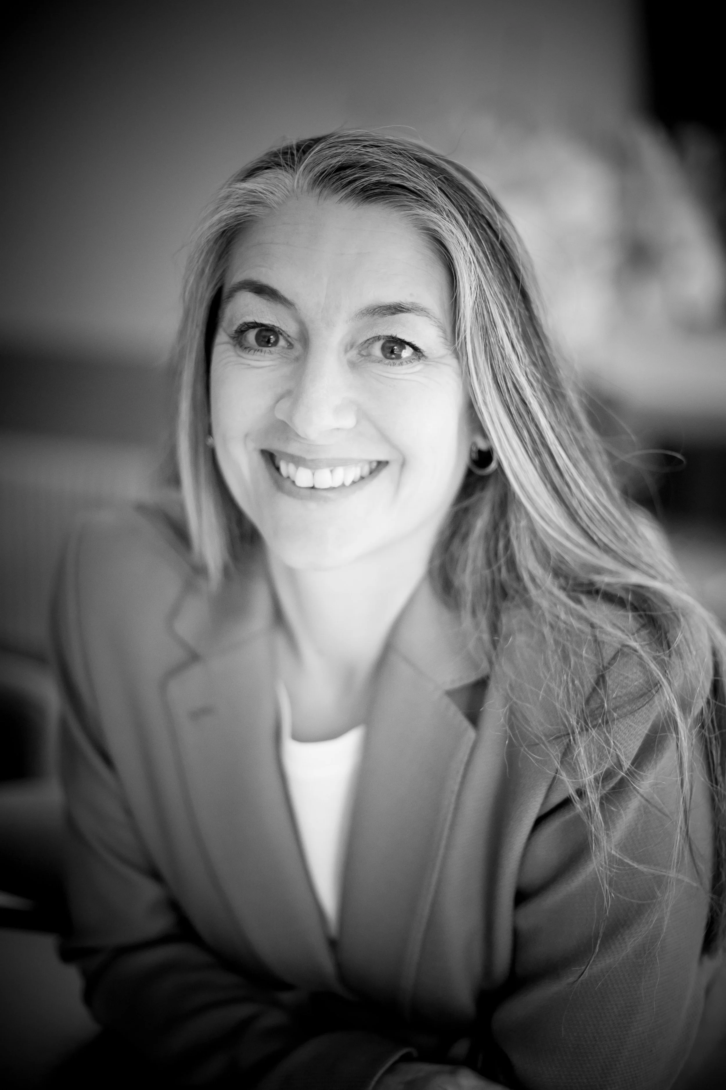 Black and white portrait of a smiling woman with long, wavy hair, wearing earrings and a blazer.