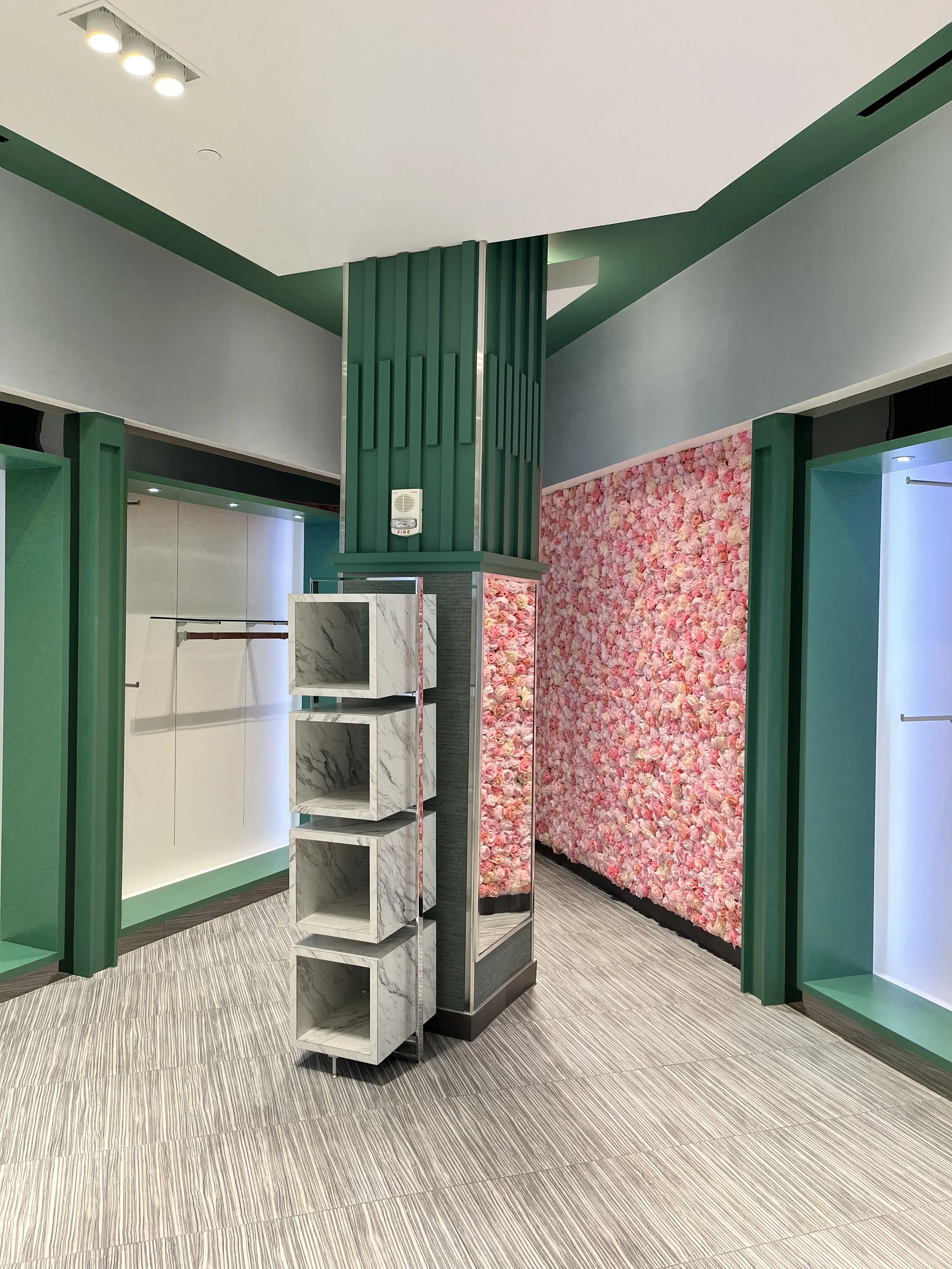 Interior of a retail store with green and pink decor, pink floral wall, marble display shelves, and gray flooring.