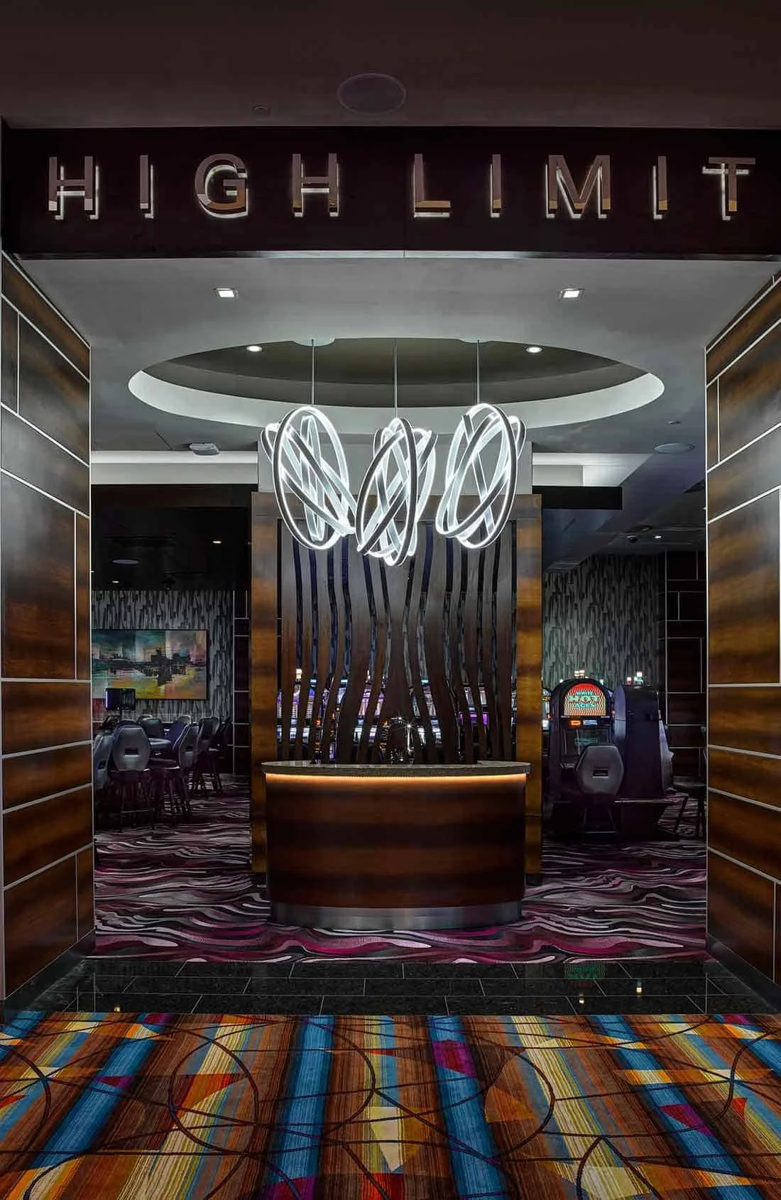 Lobby with the sign 'High Limit', modern lighting fixture, wooden paneling, and slot machines in the background.