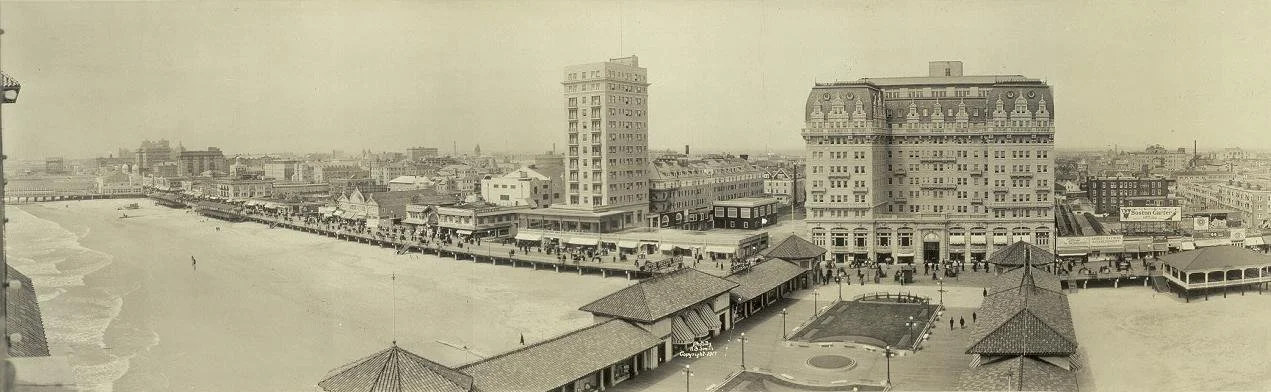 Historic Atlantic City black and white beachside scene with large buildings, a boardwalk, and beachfront structures from an earlier era.