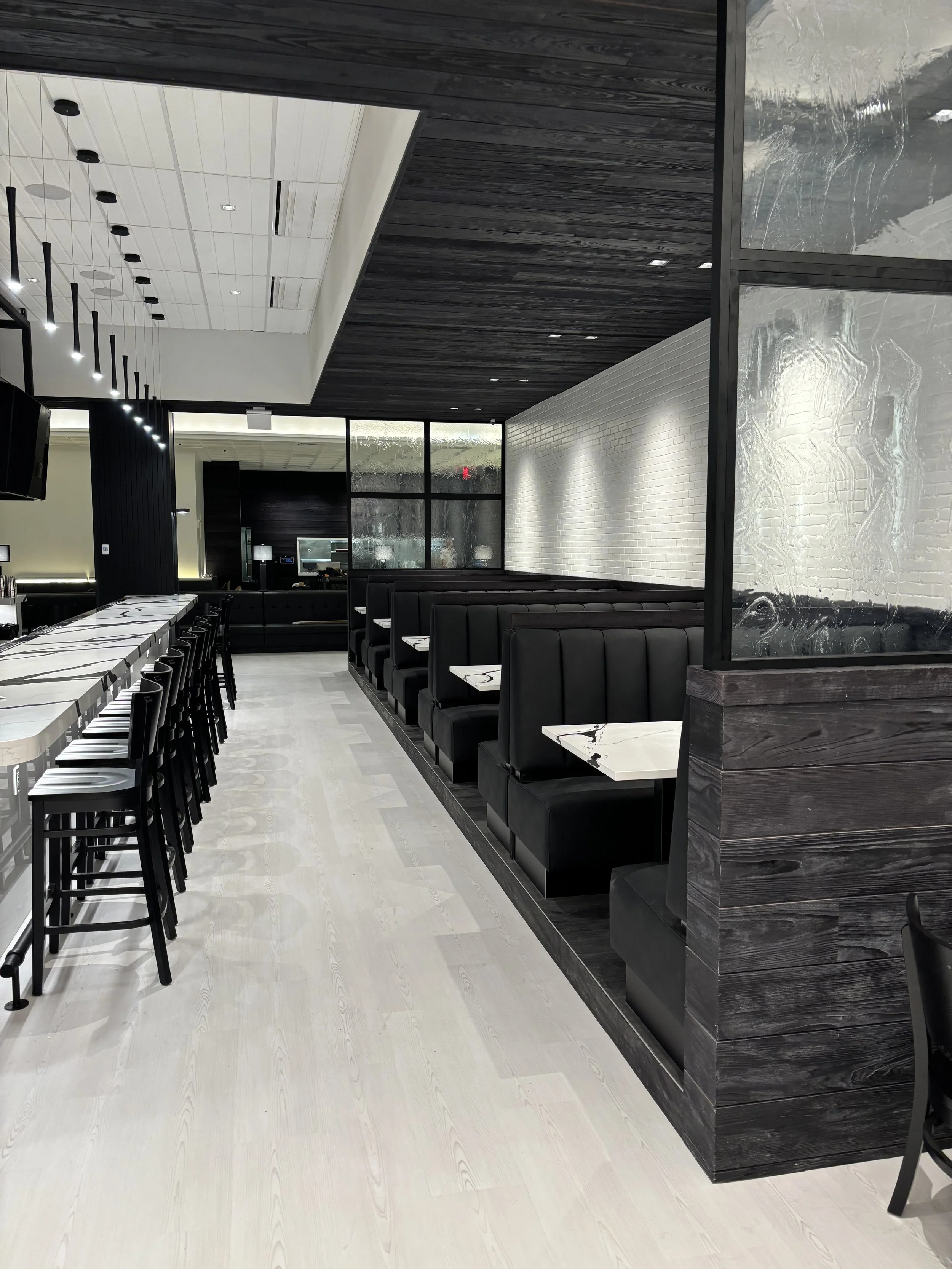 Modern restaurant interior with black booths, white marble tables, and bar seating.