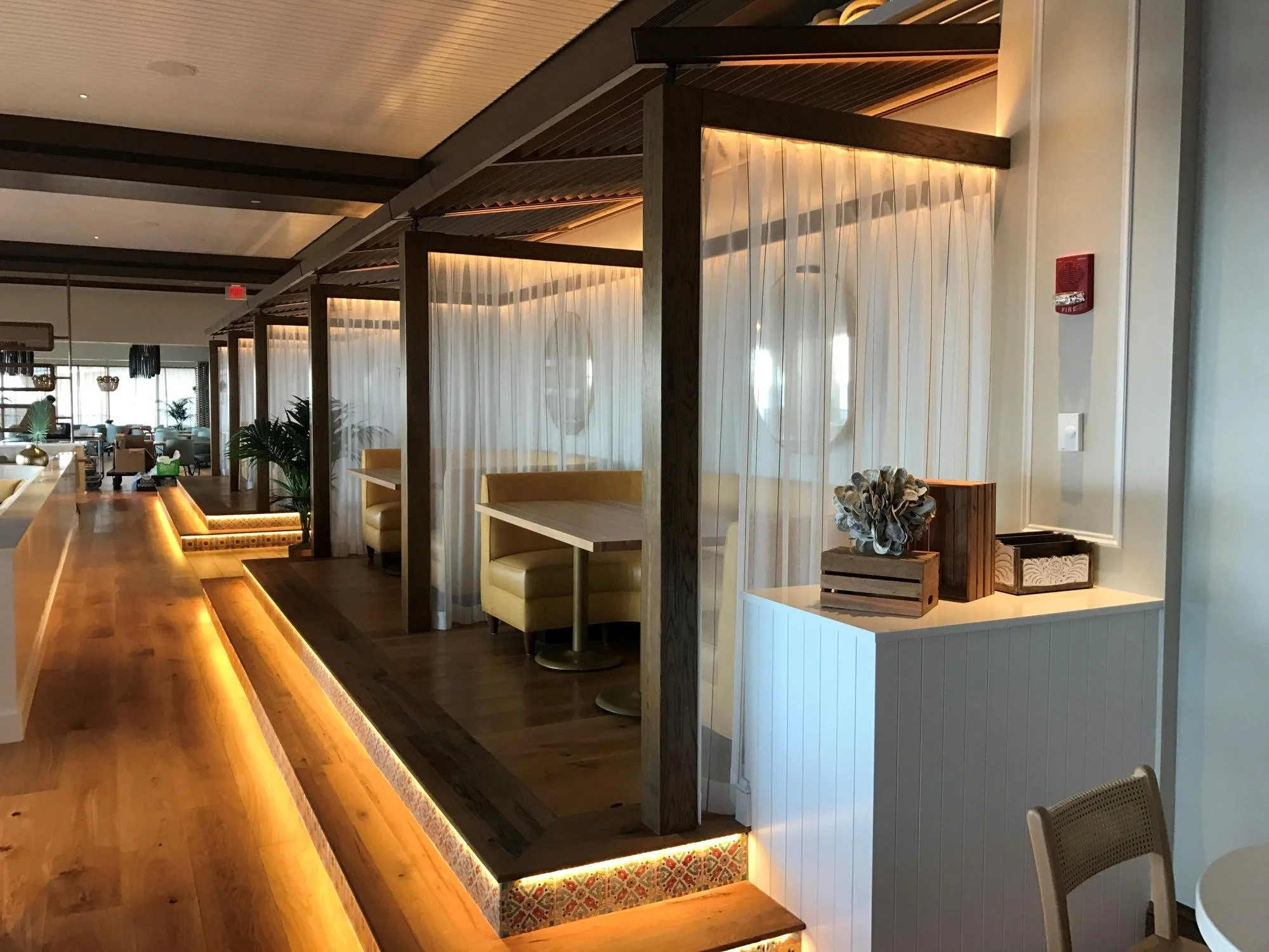 Interior of a restaurant or cafe with semi-private booth seating, yellow booths, wood accents, and warm lighting.