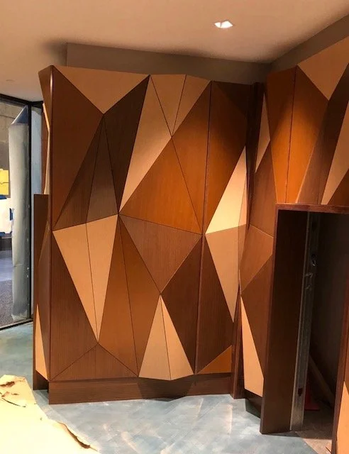 Interior view of a modern wooden wall with geometric, angular paneling in various shades of brown.