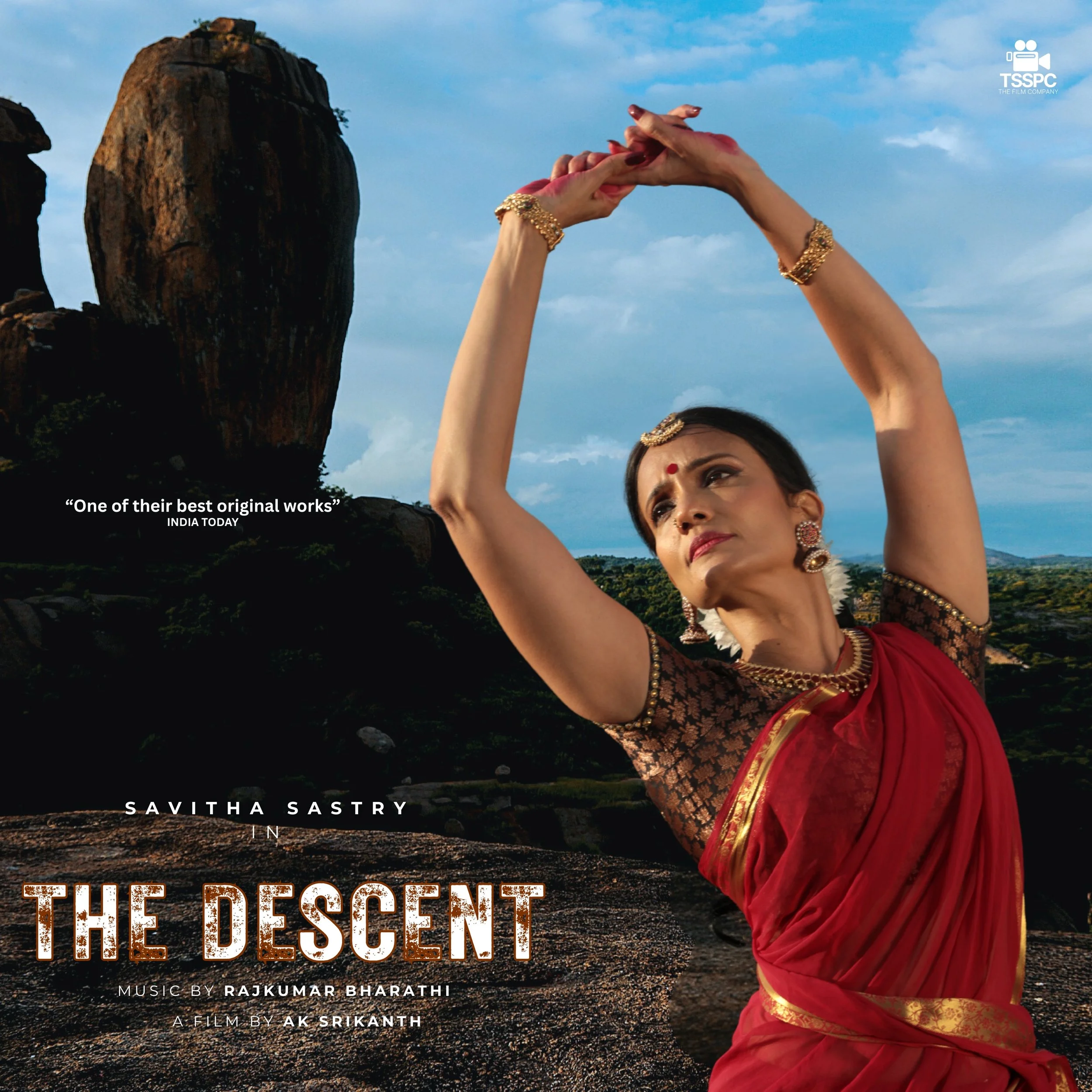 A woman in traditional Indian saree and jewelry striking a dance pose outdoors with rocky landscape and a large rock formation in the background.