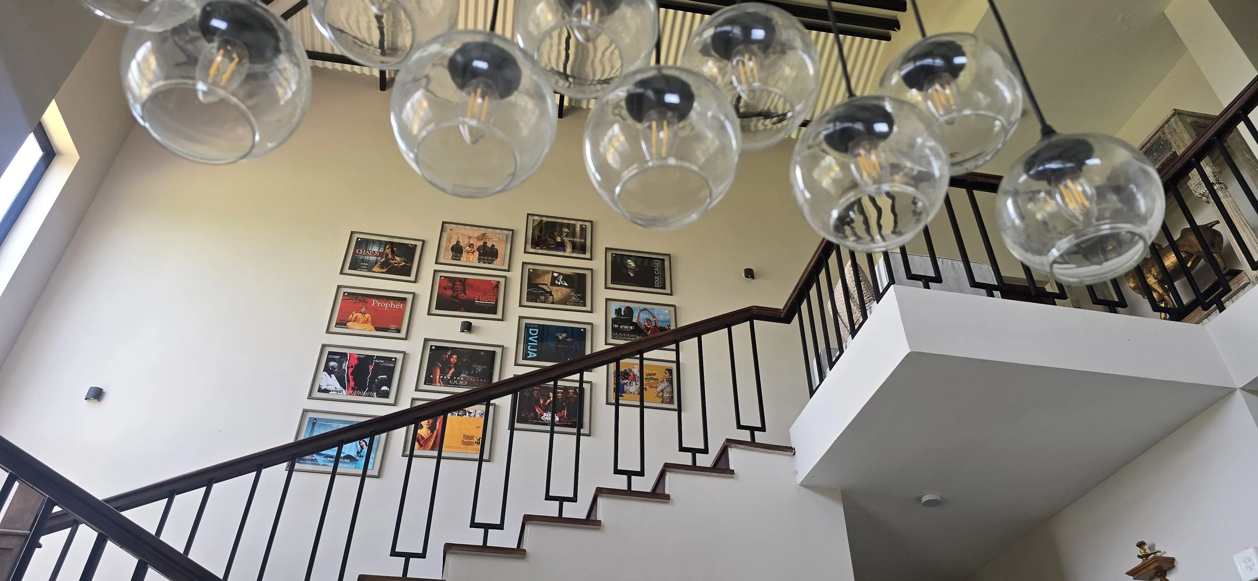Interior view of a staircase with framed pictures on the wall, glass globe chandelier hanging from the ceiling, and a window on the left side.