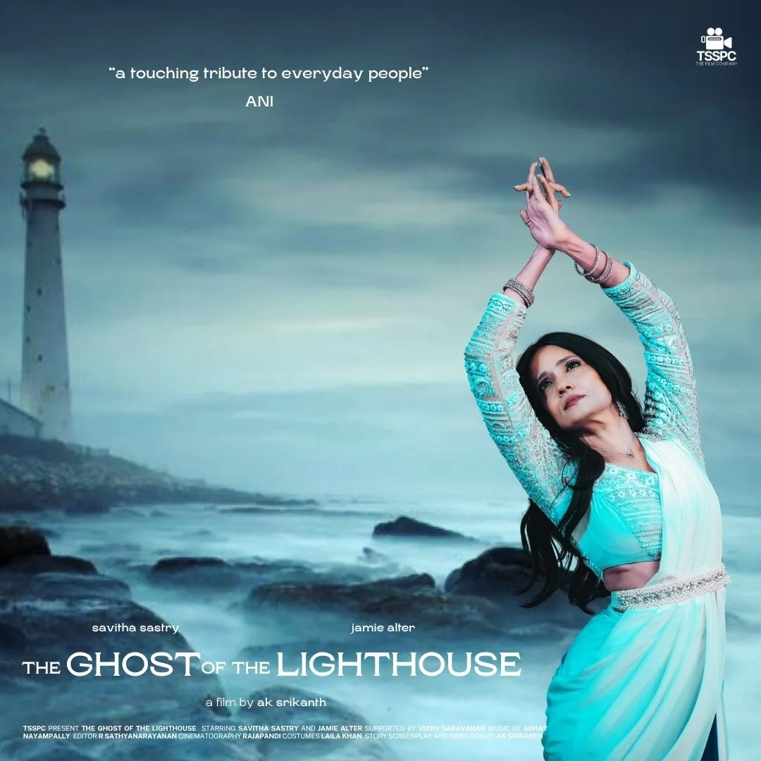 A woman in a light blue and white saree performing a dance pose with her arms extended upward against a backdrop of a lighthouse and a stormy sea.