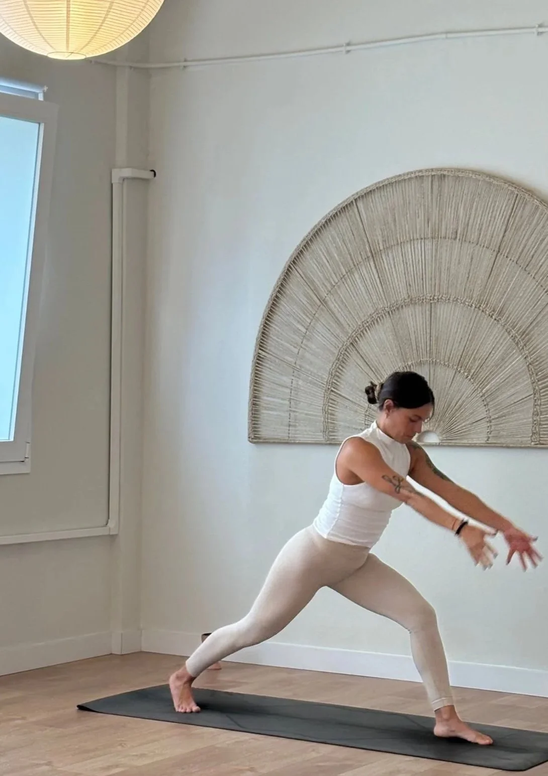 Mujer practicando yoga en una habitación con pared decorada con un arco de mimbre