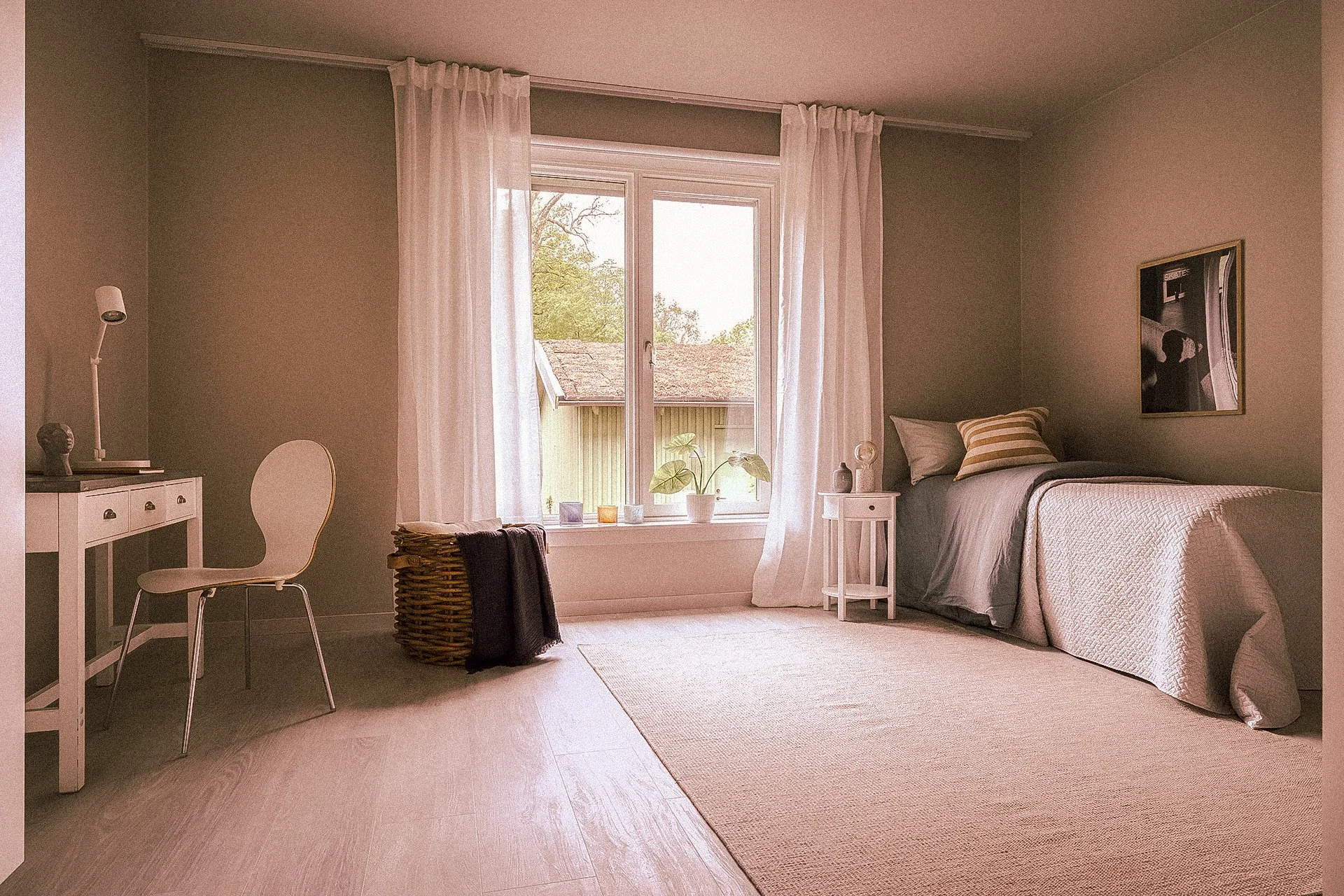 Ett ljust sovrum med ett fönster, vitt gardin, en säng med ljusgrå och vita sängkläder, en liten nattduksbord, ett växthus i fönstret med gröna växter, en vit stol och ett skrivbord med en lampa.