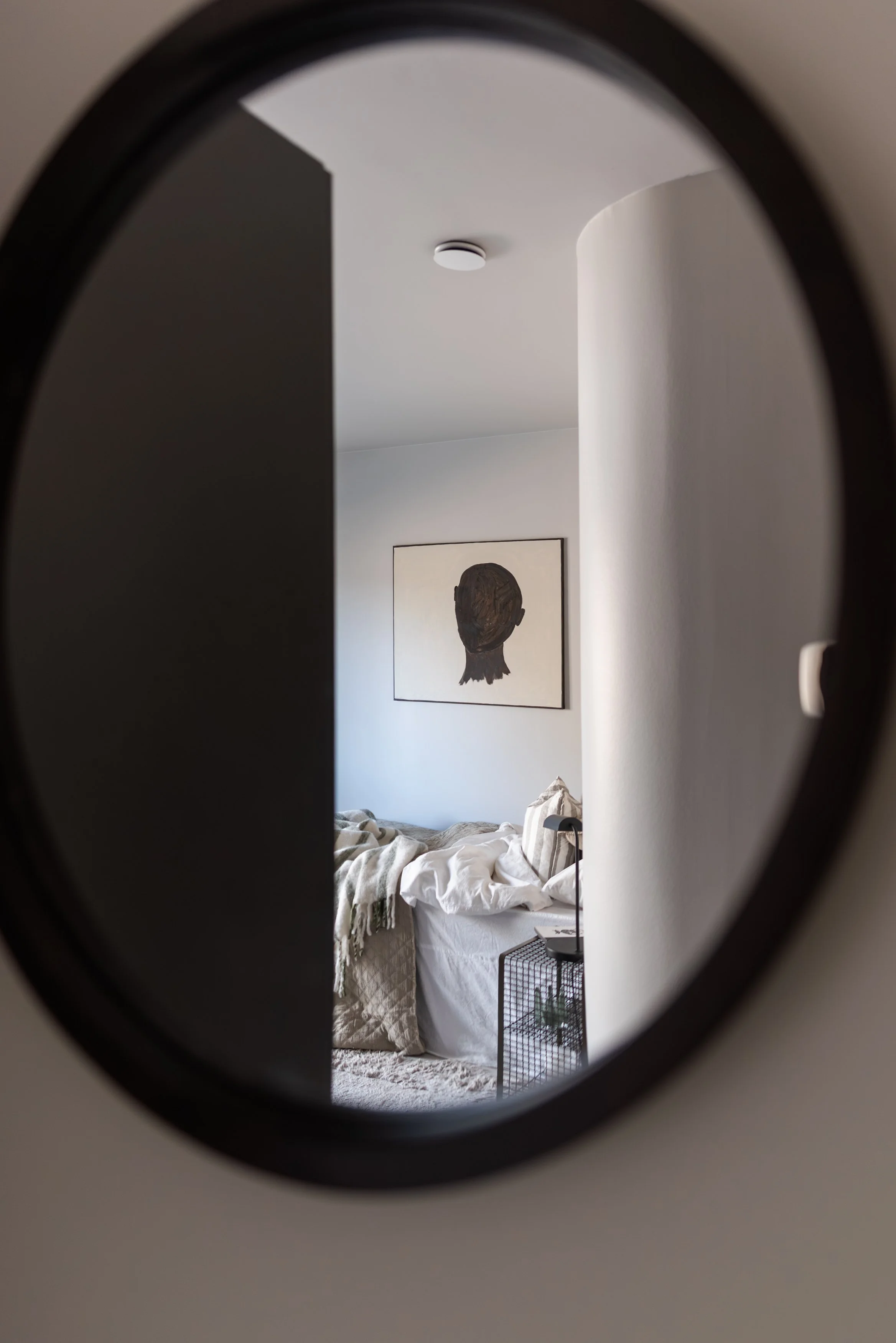 Spegellöst rum med en säng, en bild på en person, ungefär en siluett, och ett sidobord med en liten växt, ett foto av ett porträtt på väggen.
