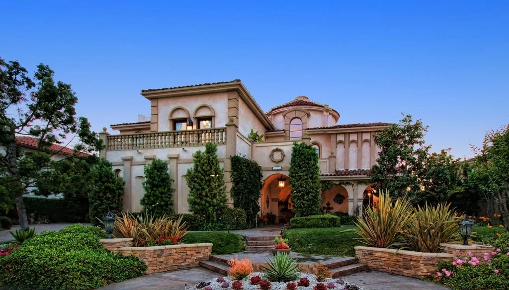Front view of a large Mediterranean-style house with a garden and landscaped walkway.