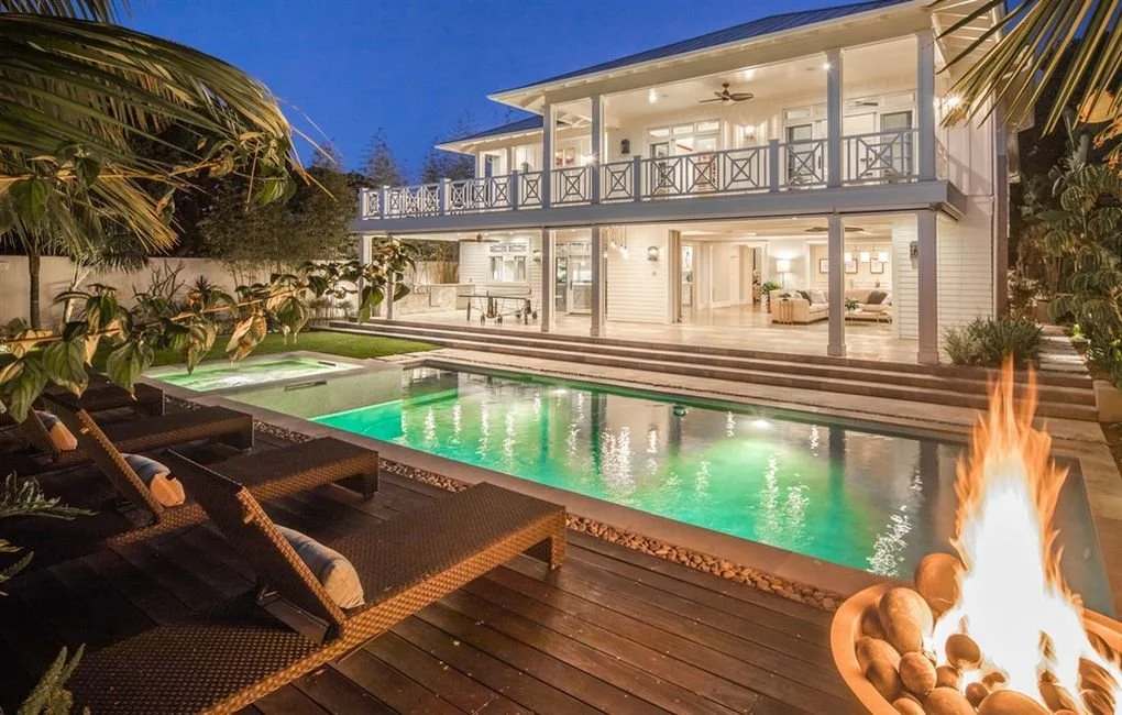 Luxury house with a swimming pool, outdoor seating, and a fire pit in a tropical setting during evening.