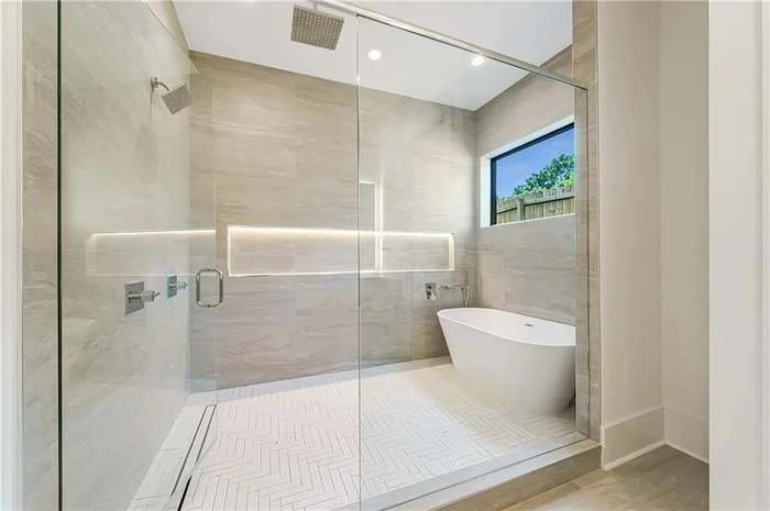 Modern bathroom with a walk-in shower, a freestanding bathtub, and a large window overlooking an outdoor area.