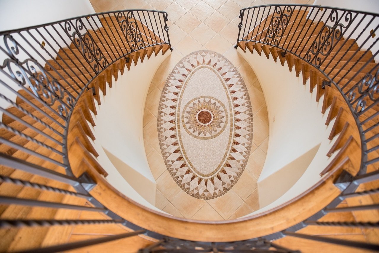 View looking down from the top of a spiral staircase with a decorative design on the floor below.