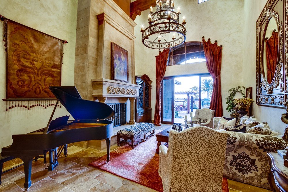 Living room with a grand piano, ornate fireplace, plush sofa, armchairs, chandelier, large window with curtains, and decorative wall art.