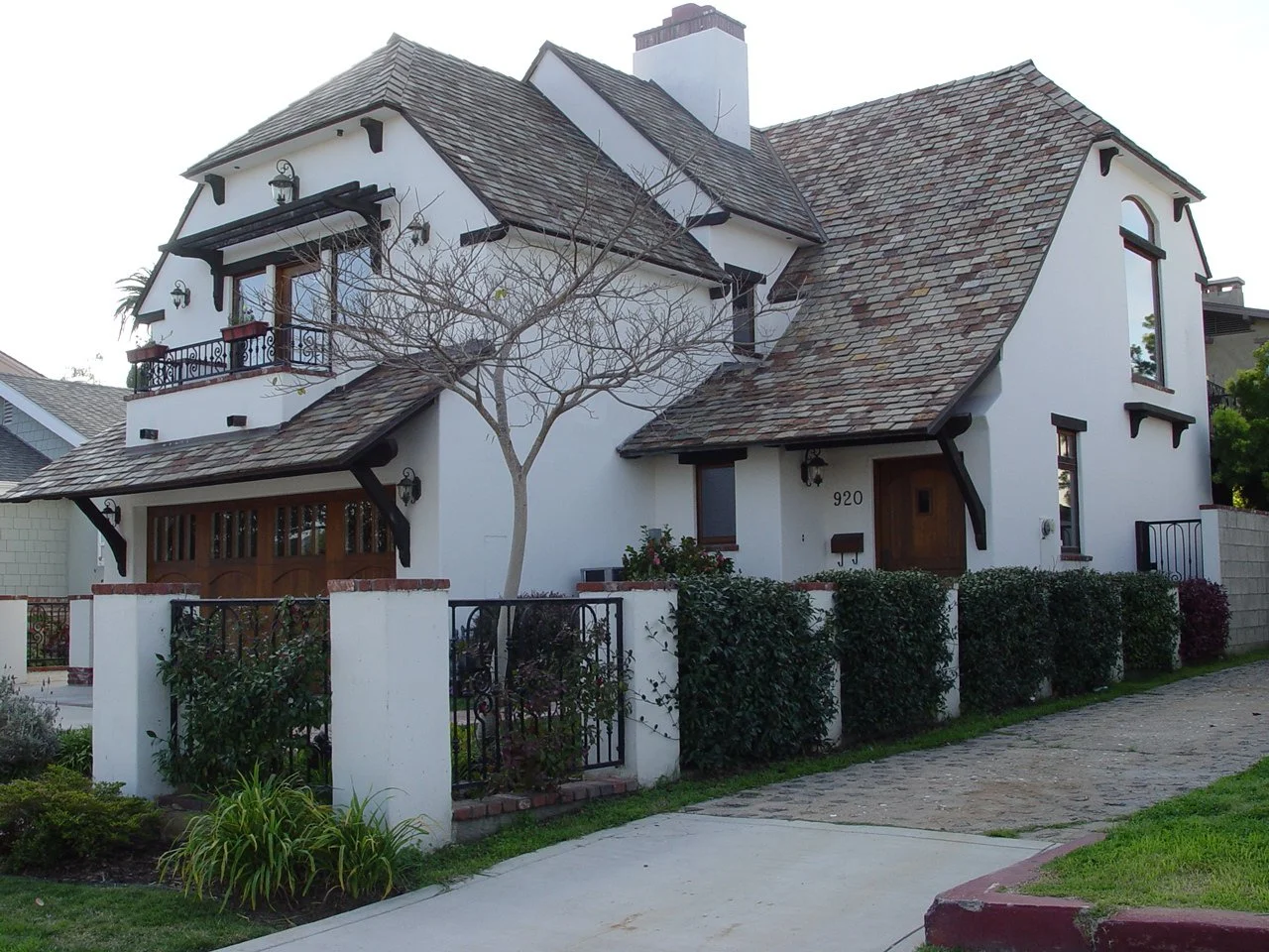 A large white house with a tiled roof, black trim, and a small front yard with bushes and a leafless tree.