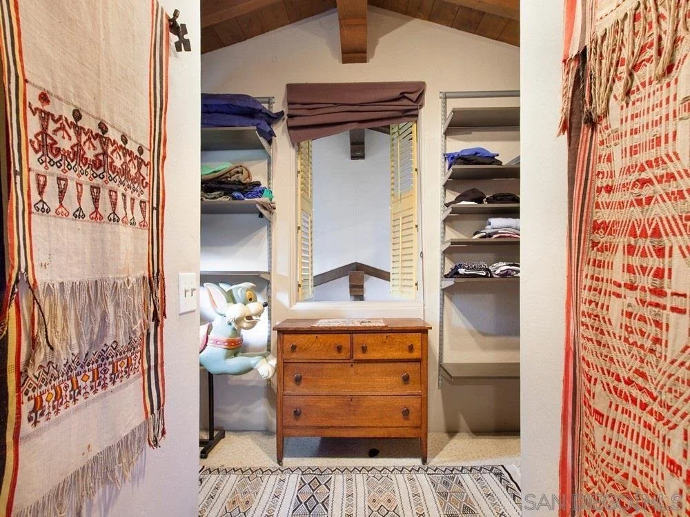 A small dressing area with a wooden dresser, a mirror, and shelves filled with folded clothes. Two decorative textiles hang on either side of the entrance, and a large rocking horse toy is visible on the left side.