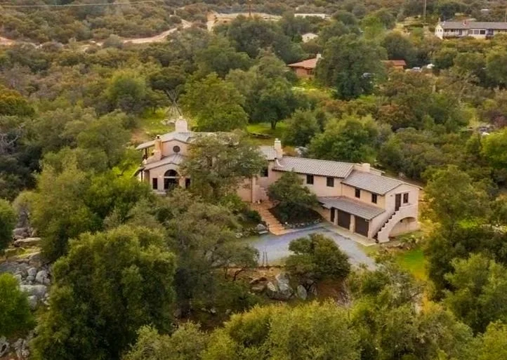 A large house with Spanish-style architecture, surrounded by trees and located in a hilly area.