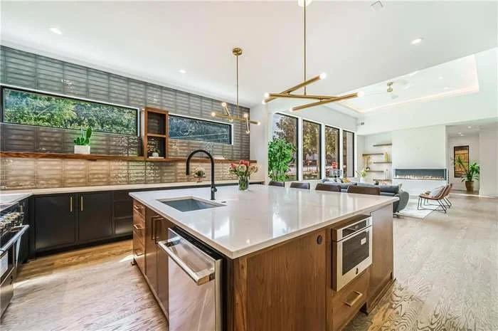 Modern open-concept kitchen with a large island, black lower cabinets, wooden accents, and seating area with a living room in the background.
