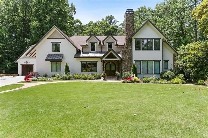 Large modern house with white exterior, multiple gabled roofs, a chimney, and well-maintained front lawn with landscaping.