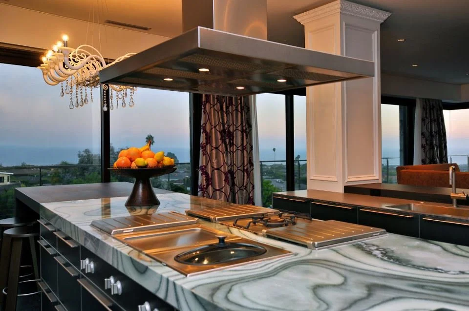 Modern kitchen with a marble island, a fruit bowl, and a view of the outdoors through large windows.