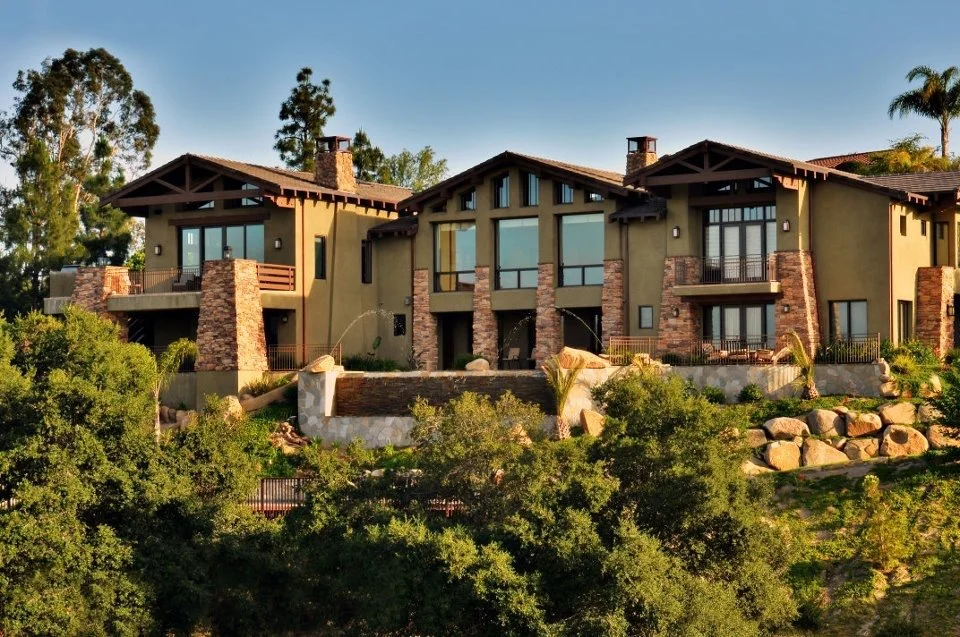 Luxury modern house on a hillside surrounded by trees and rocks, with large windows and a balcony.