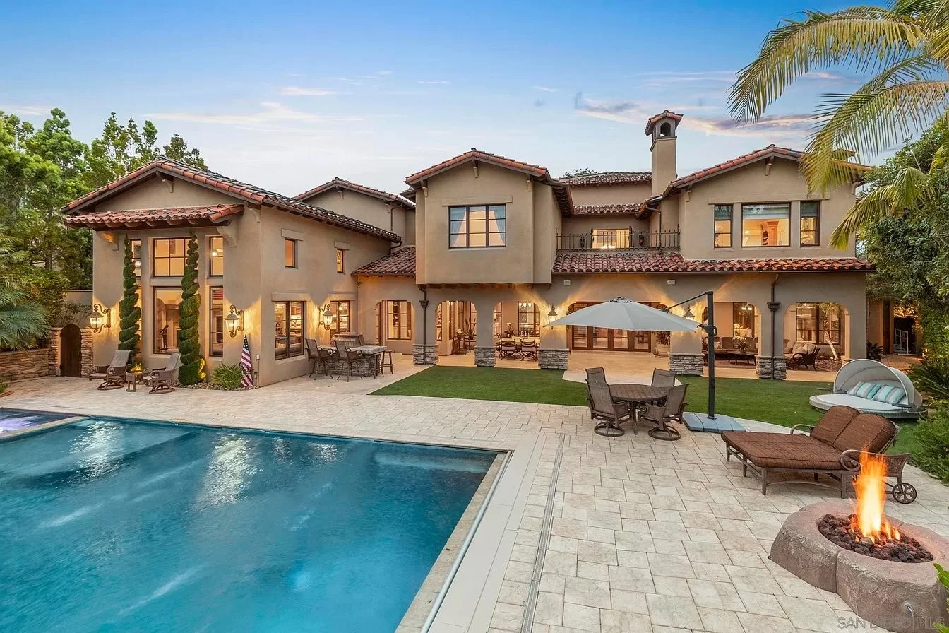 Luxury two-story house with a swimming pool, patio furniture, and a fire pit in the backyard during sunset.