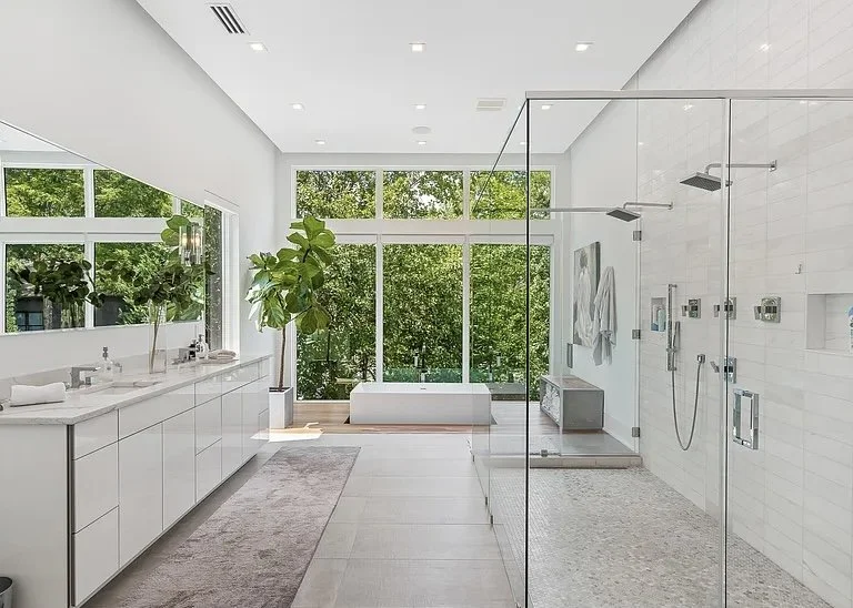Modern spacious bathroom with large windows, white cabinets, and a glass shower enclosure.