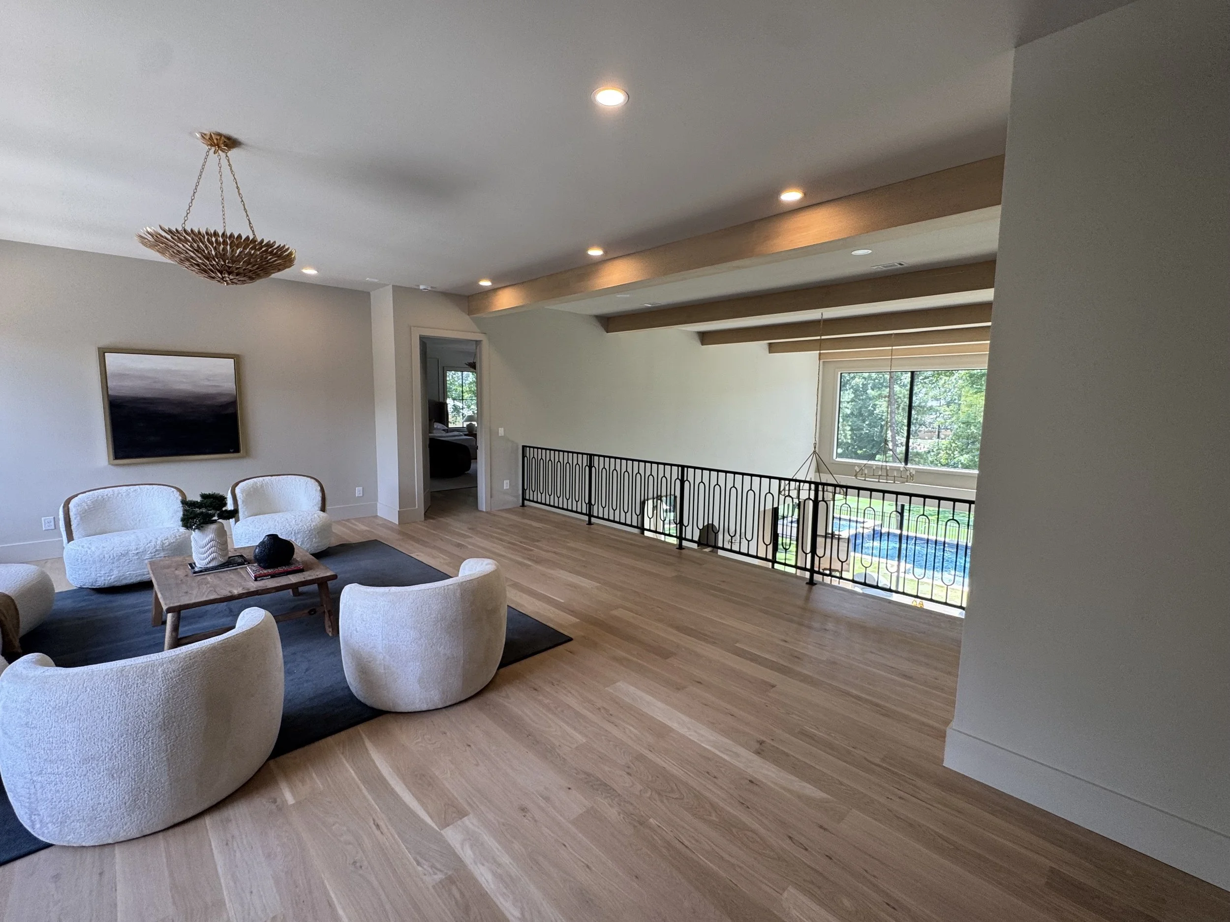 Open-concept living room with white armchairs, a coffee table, a wall-mounted painting, large window, and wooden floors.