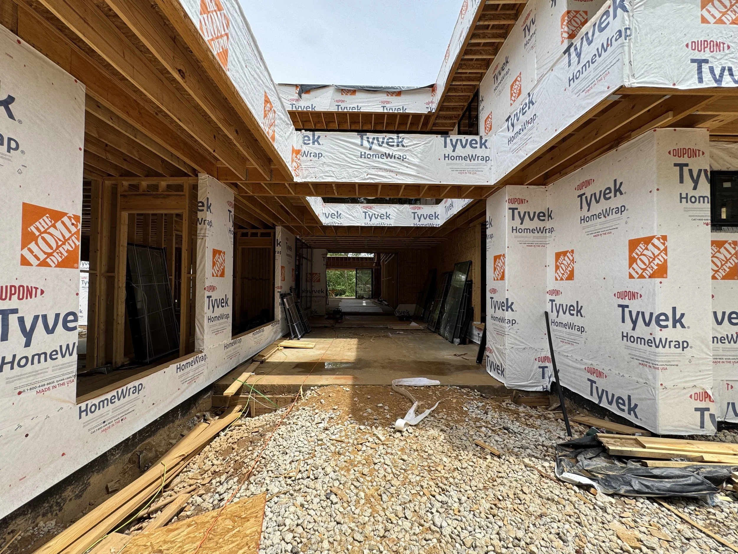 Construction site with wooden framing and Tyvek HomeWrap installed on the exterior walls and ceiling, with an open sky above.