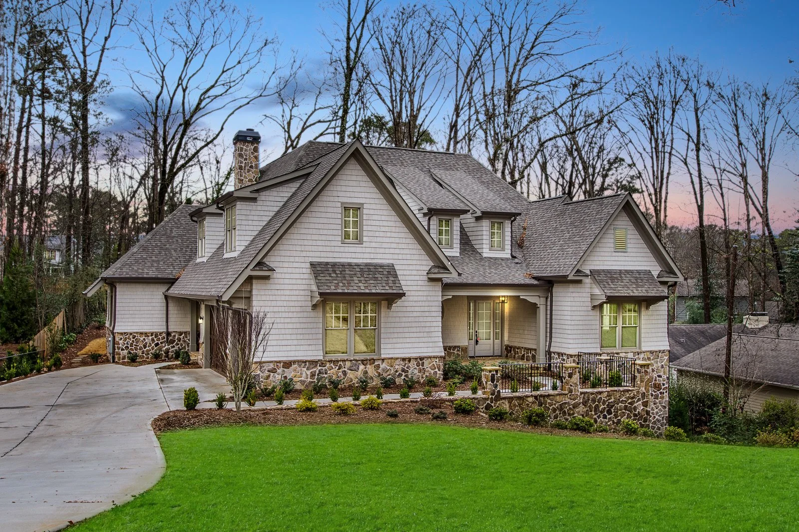 A large two-story house with stone accents on the lower part of the exterior, surrounded by a well-manicured lawn and leafless trees in the background at dusk.