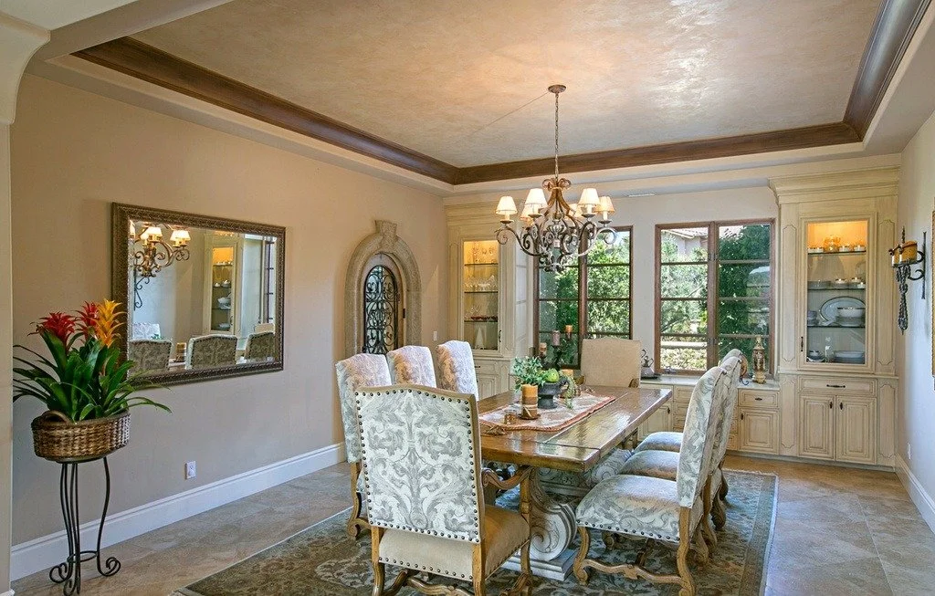 Dining room with a wooden table, six upholstered chairs, a chandelier, a large window, and built-in cabinets with glass doors.