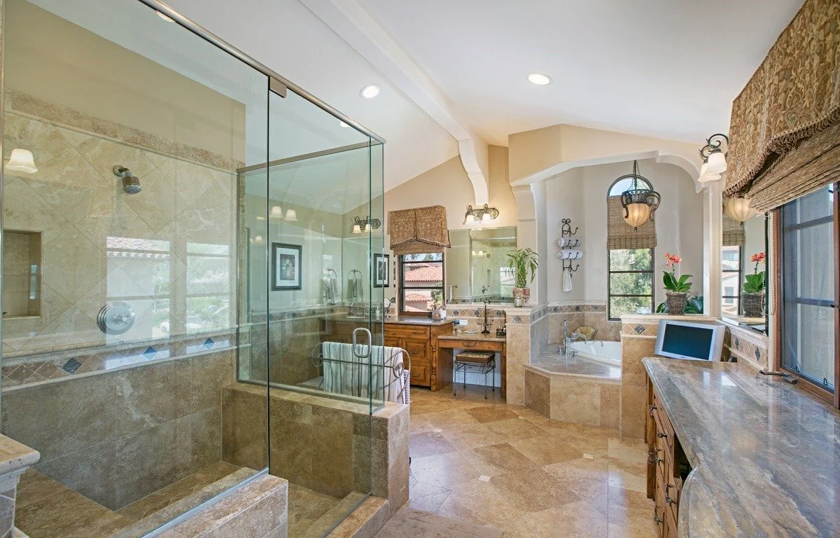 Luxury bathroom with glass-enclosed shower, bathtub, wooden vanity, large mirrors, potted plants, and windows with curtains.