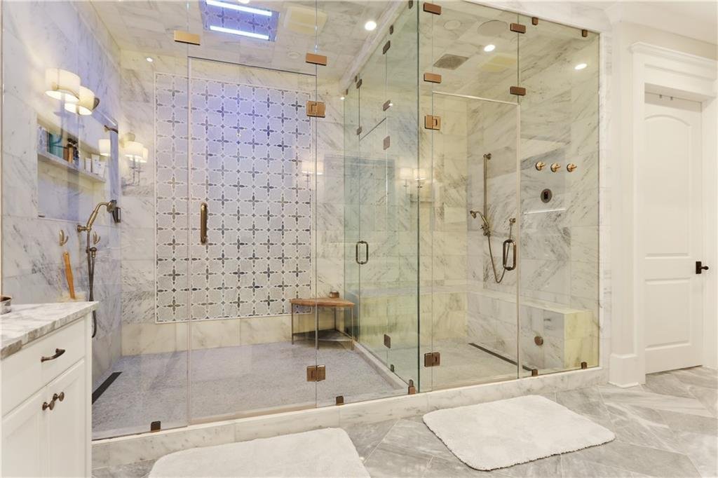 A luxurious bathroom with a large glass-enclosed shower featuring marble walls and a built-in bench, white towels on the floor, and a white cabinet with a marble countertop.