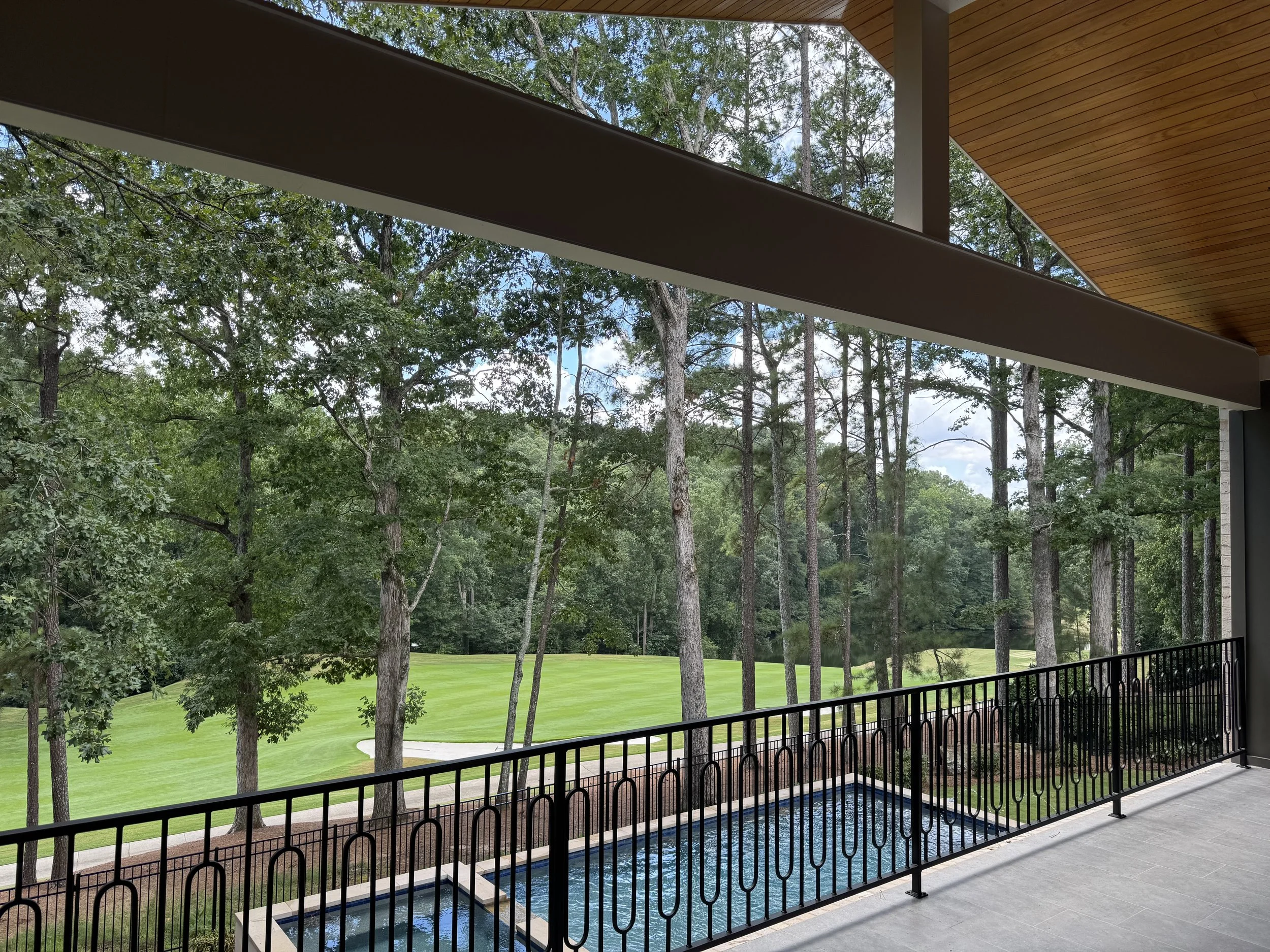 View from a balcony showing a green grassy area, trees, and a partly cloudy sky.