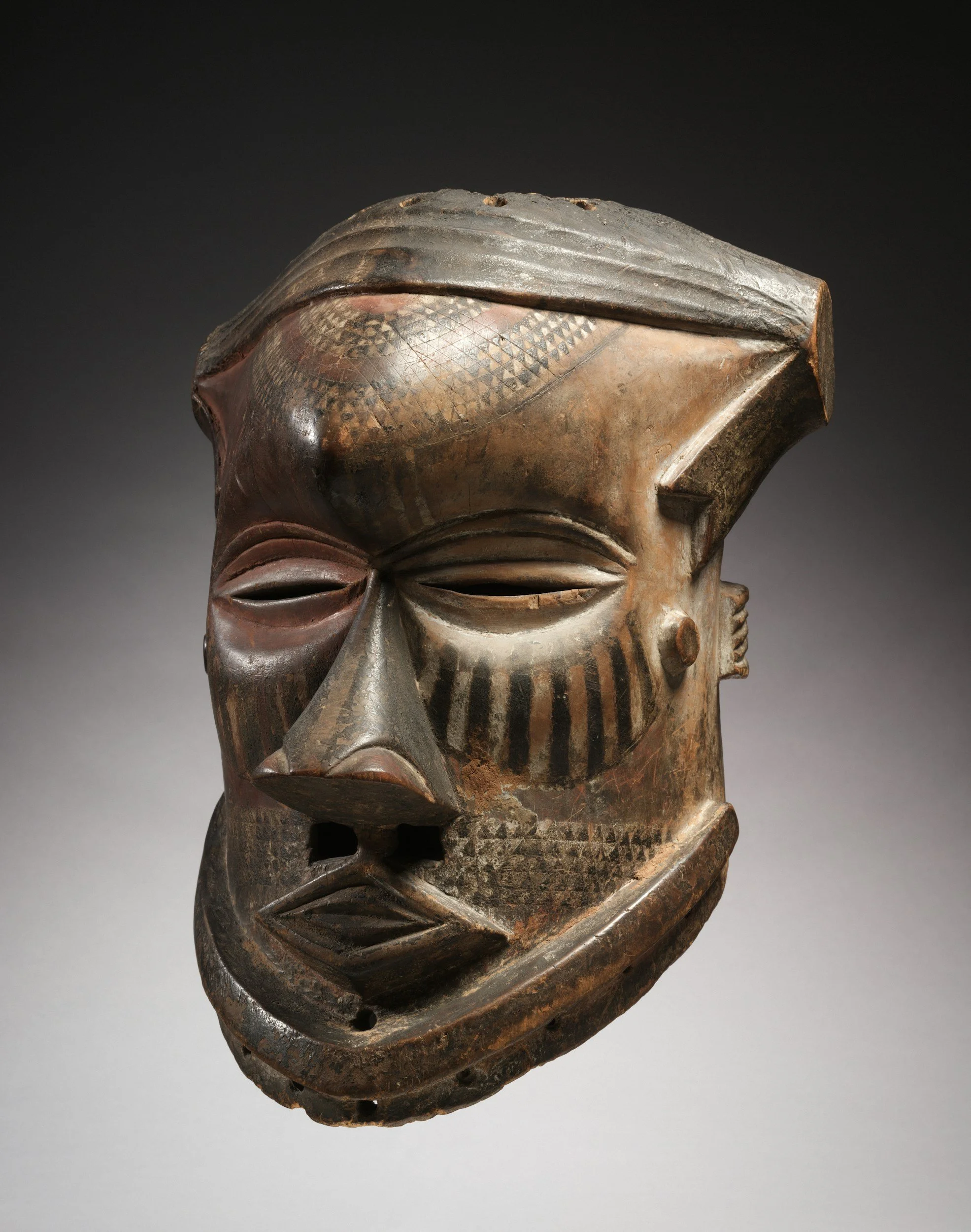 Close-up of a wooden African tribal mask with carved facial features and intricate patterns, dark background.