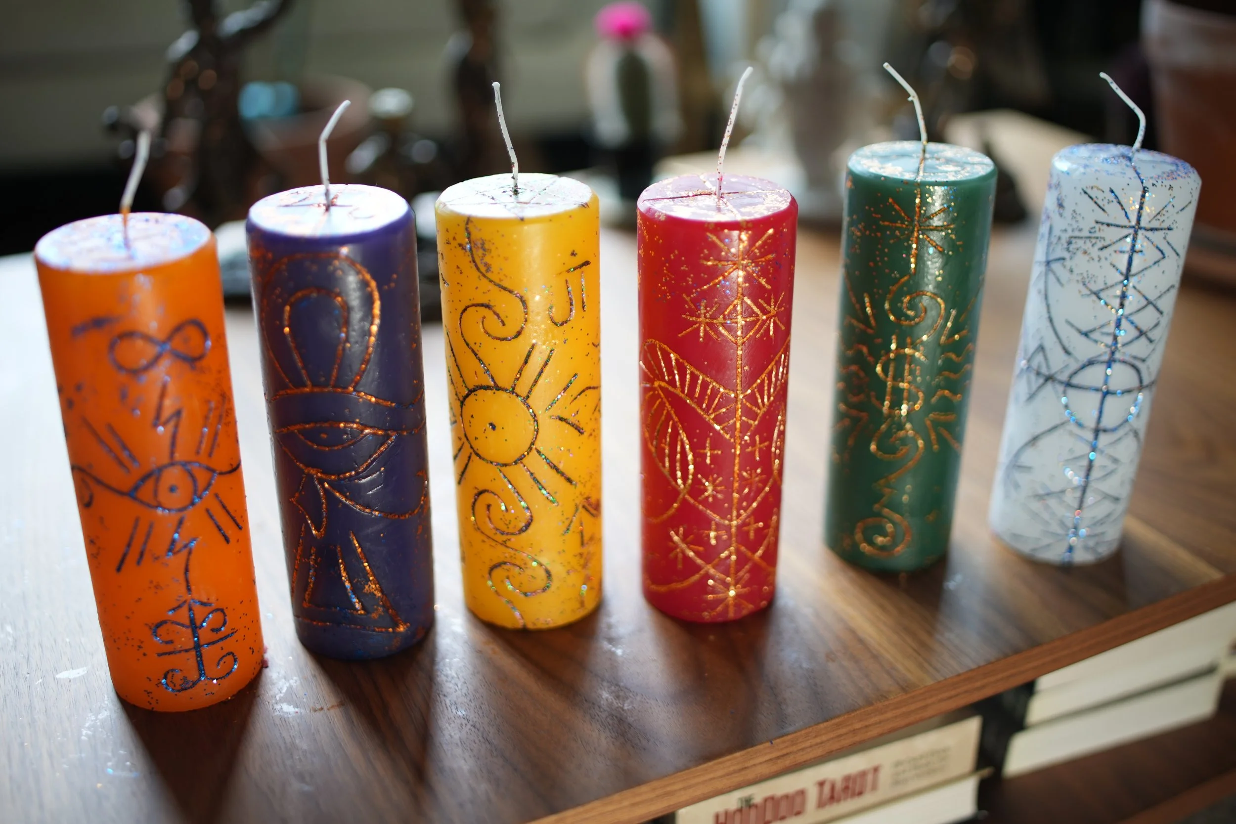 Six colorful candles with gold and glitter designs, arranged in a row on a wooden surface.