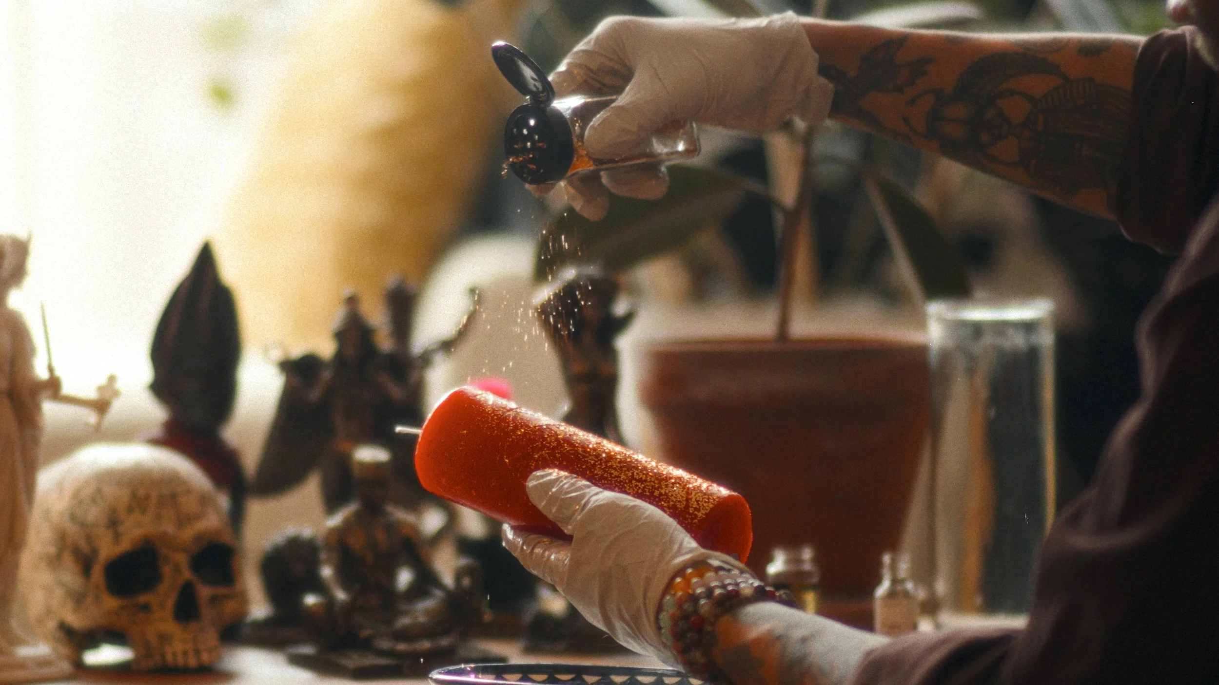 A person holding a lit match in front of a fingerless glove, with sparking particles flying off the match. In the background, various decorative skulls and figures are visible.